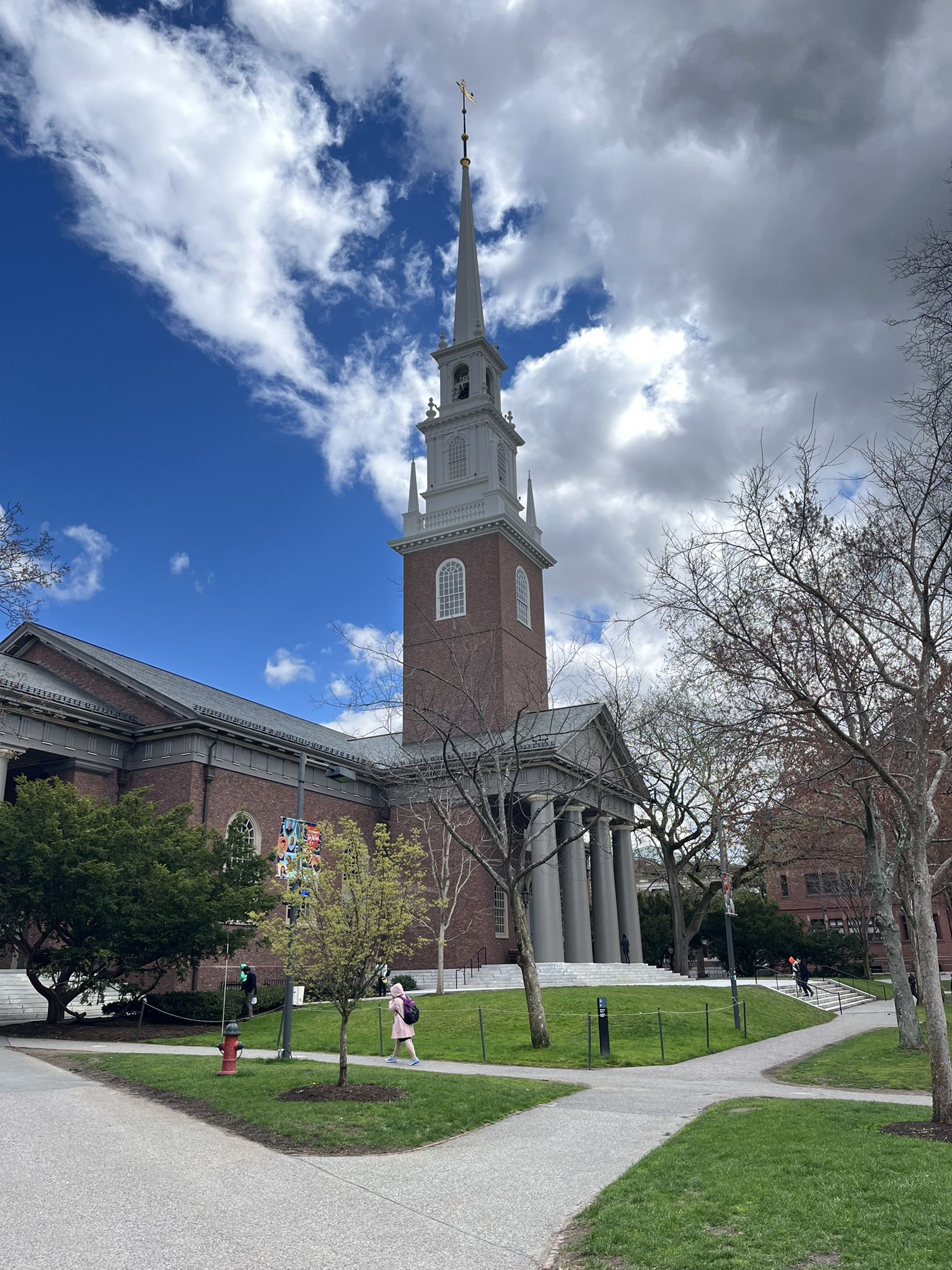 A church with a tall steeple and columns, people walk on paths. - Harvard Yard Tour