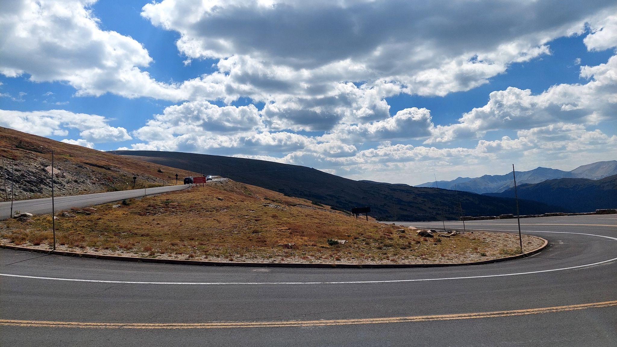 Winding paved mountain road with distant cars under a dramatic cloudy sky. - Marmot Point Trail