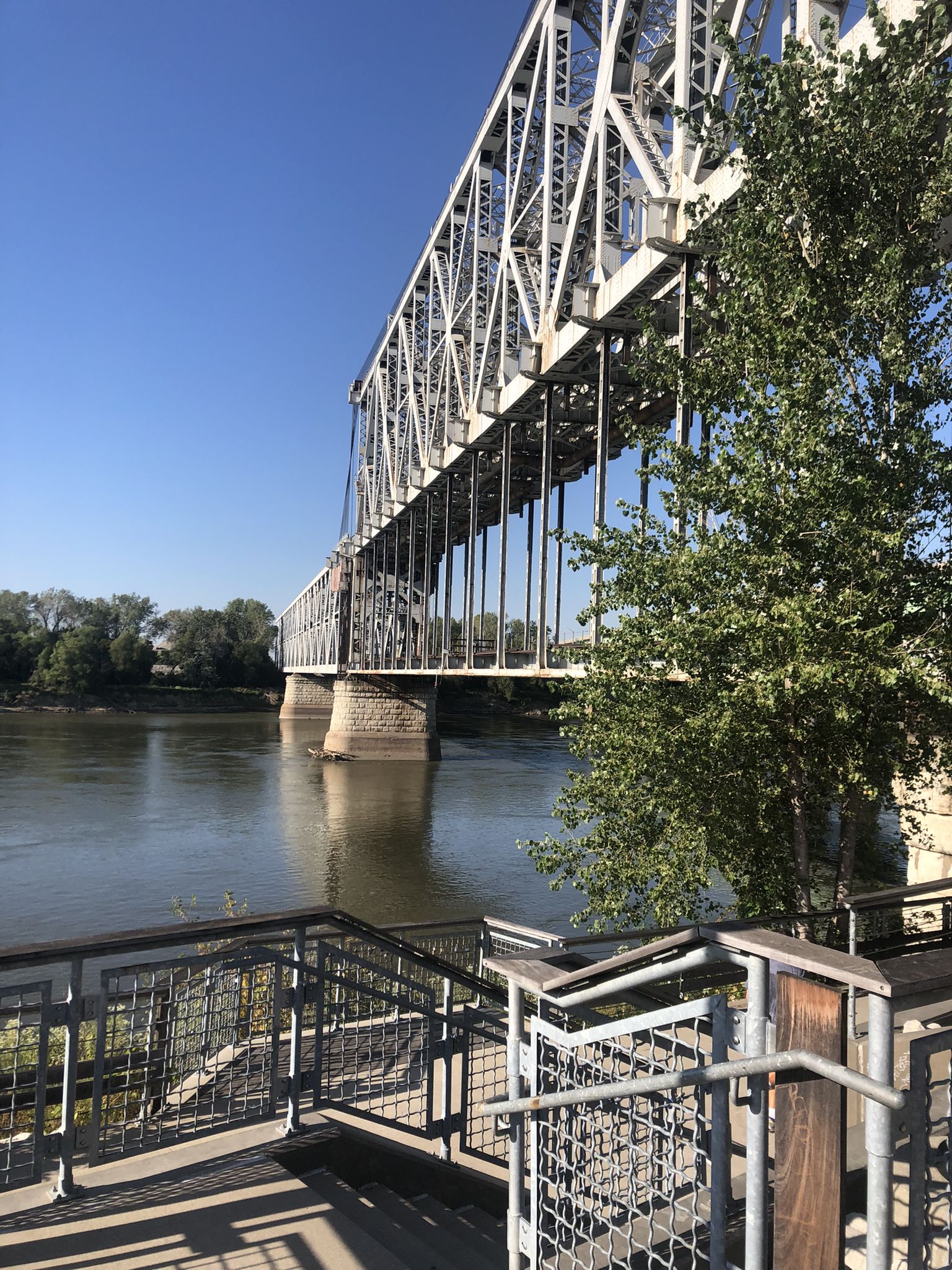 A large metal truss bridge extends over a river from a viewing platform. - Riverfront Heritage Trail