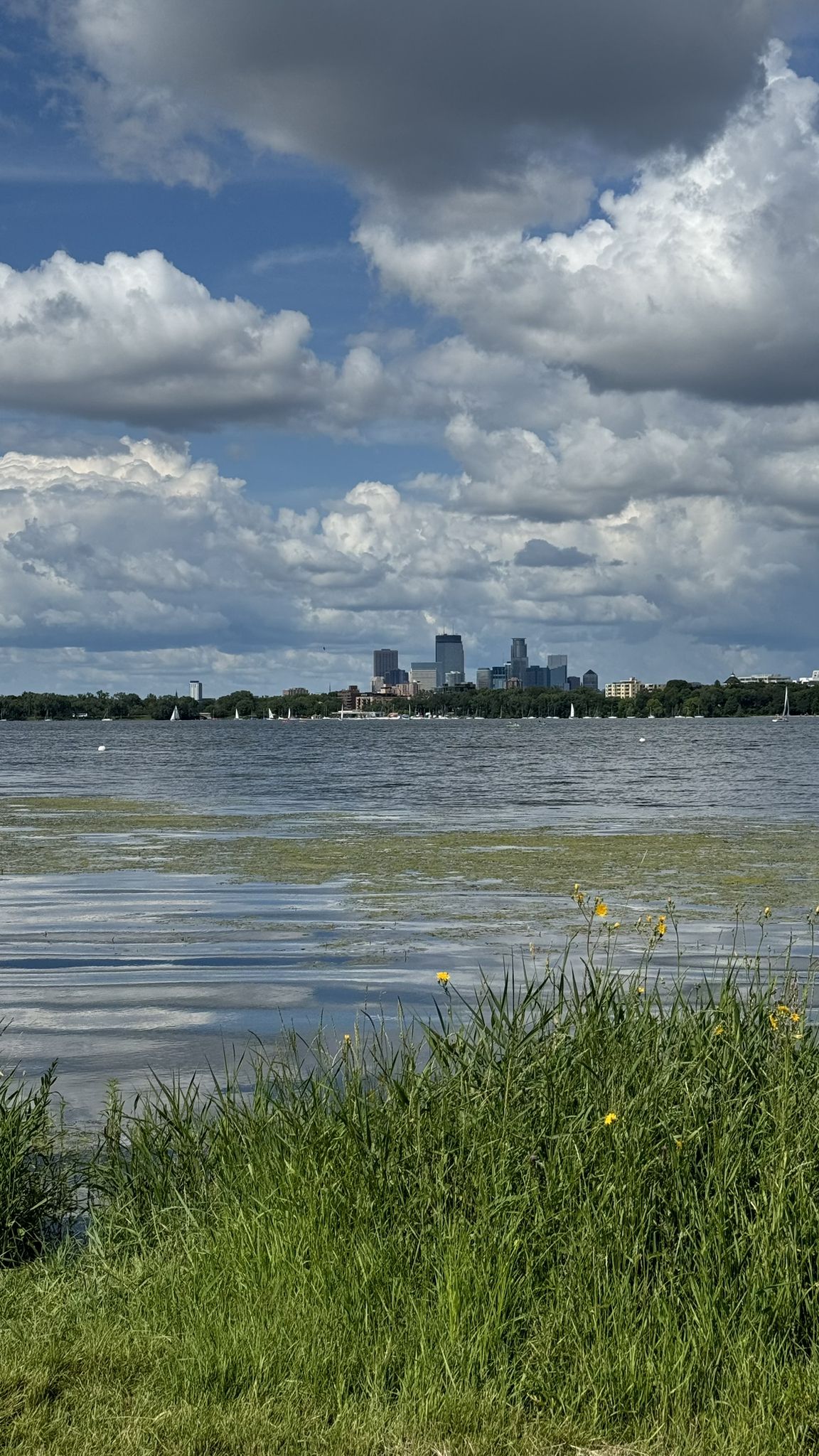 Distant city skyline across a lake with sailboats under a cloudy sky. - Chain of Lakes Loop