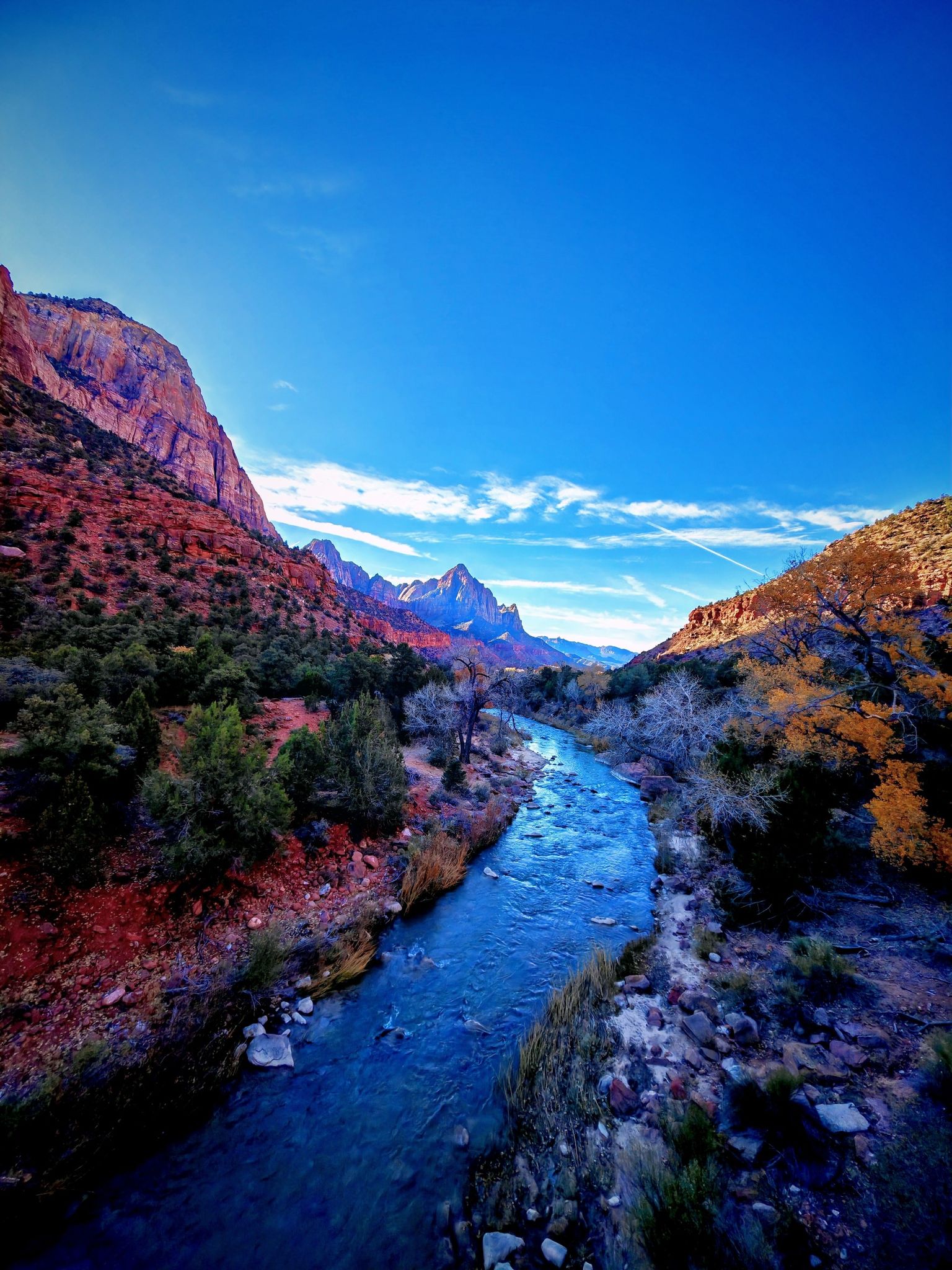 Blue river flows through a colorful canyon with red rock walls, bright sky. - View to South Mountain – Majestic View Lodge loop from Springdale