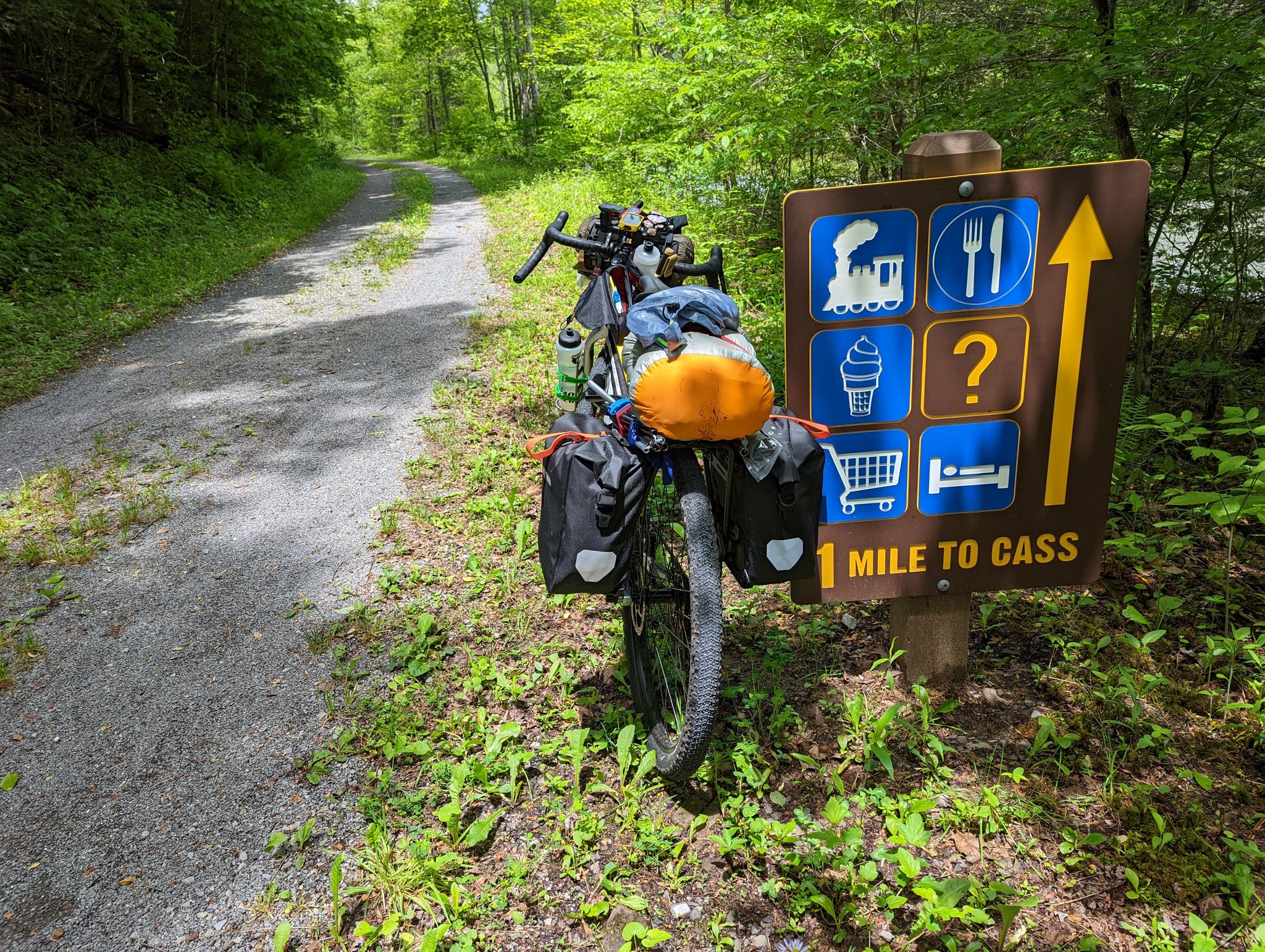 Loaded touring bicycle parked next to a trail sign on a sunny gravel path. - Greenbrier River Trail loop from Peters Mountain