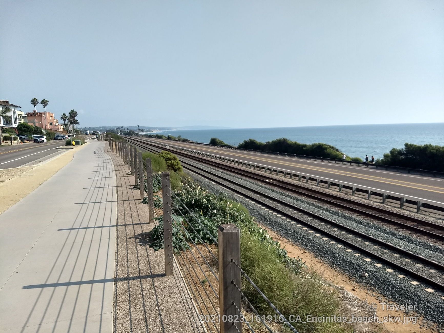 Coastal view with train tracks, a sidewalk, and the ocean under a clear sky. - Coastal Rail Trail