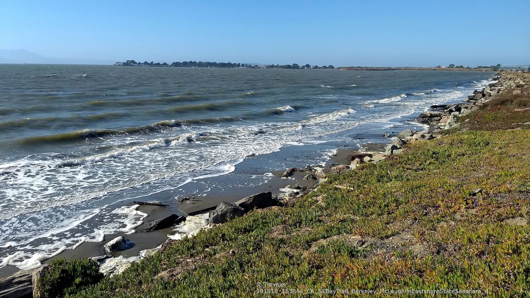 Choppy waves on a bay next to a rocky, grassy shoreline. - Aquatic Park North Trailhead – Aquatic Park loop from Emeryville