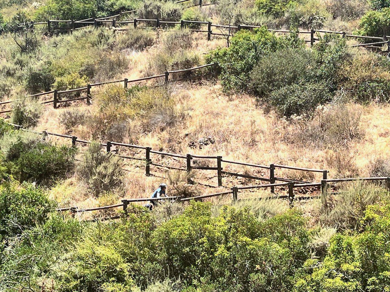 Terraced hillside with dry grass, green bushes, and wooden fences. - Santa Fe Valley Trail