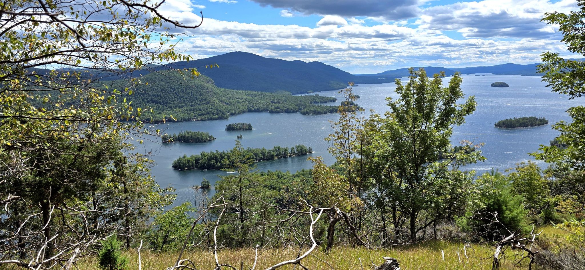 Scenic overlook of a vast lake with islands, green mountains, and cloudy sky. - Tongue Mountain Range Loop