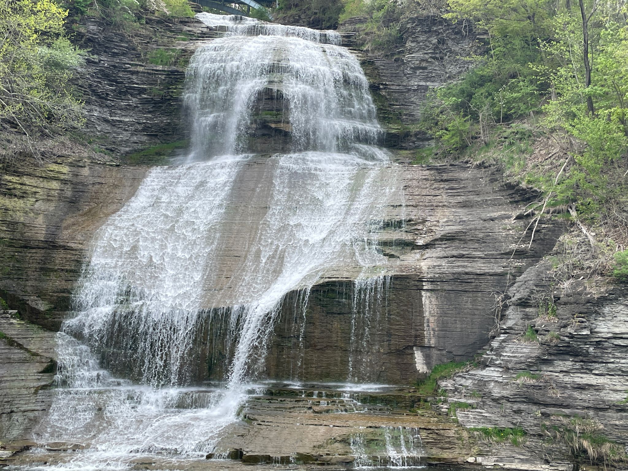 Multi-tiered waterfall cascades over rocky cliffs with green trees under bright light. - Shequaga Falls Park – Mural of Catharine Montour loop from Shequaga Falls