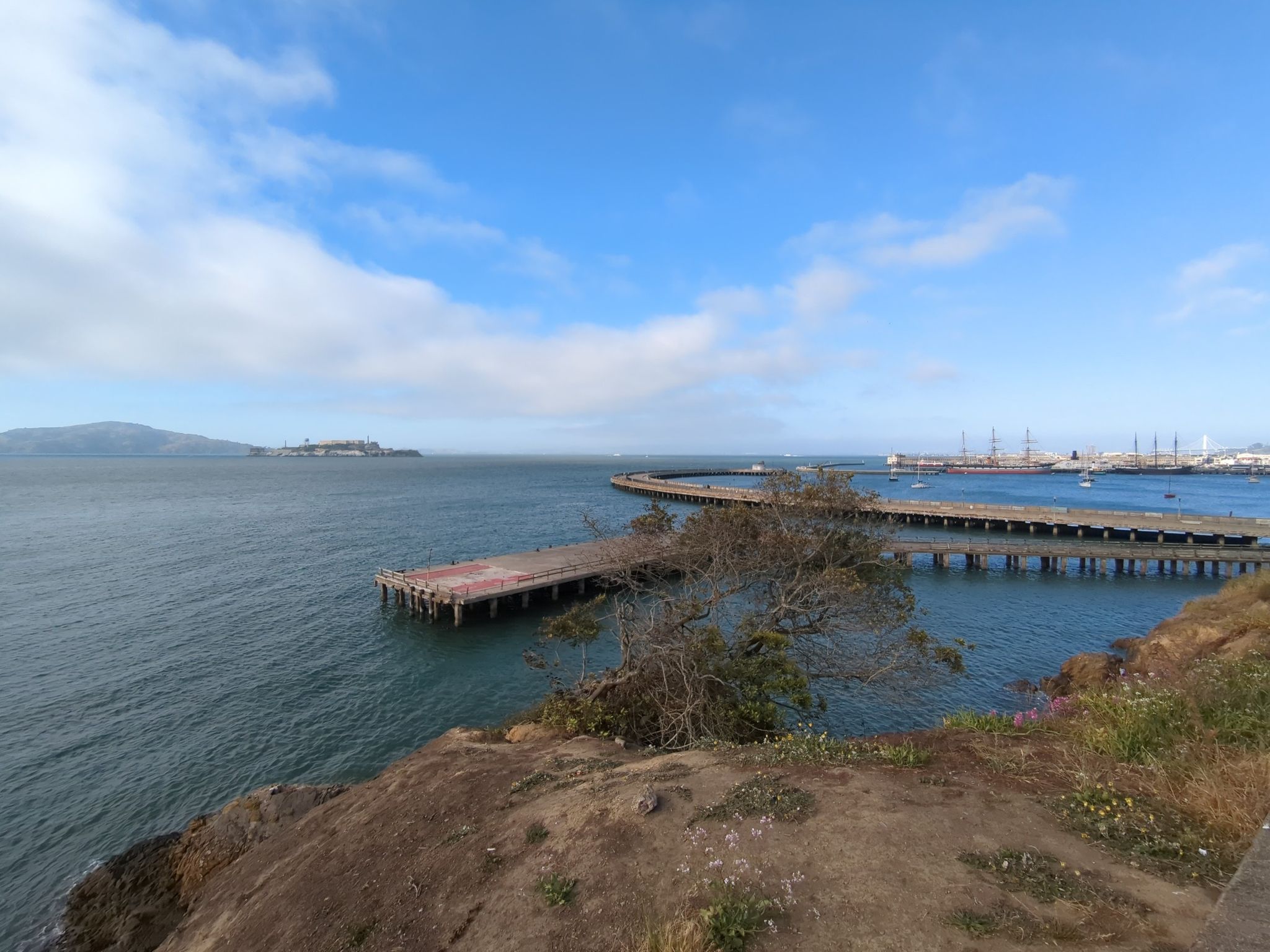 Wide bay with a long pier, distant island, and city under a blue sky. - Upper Fort Mason
