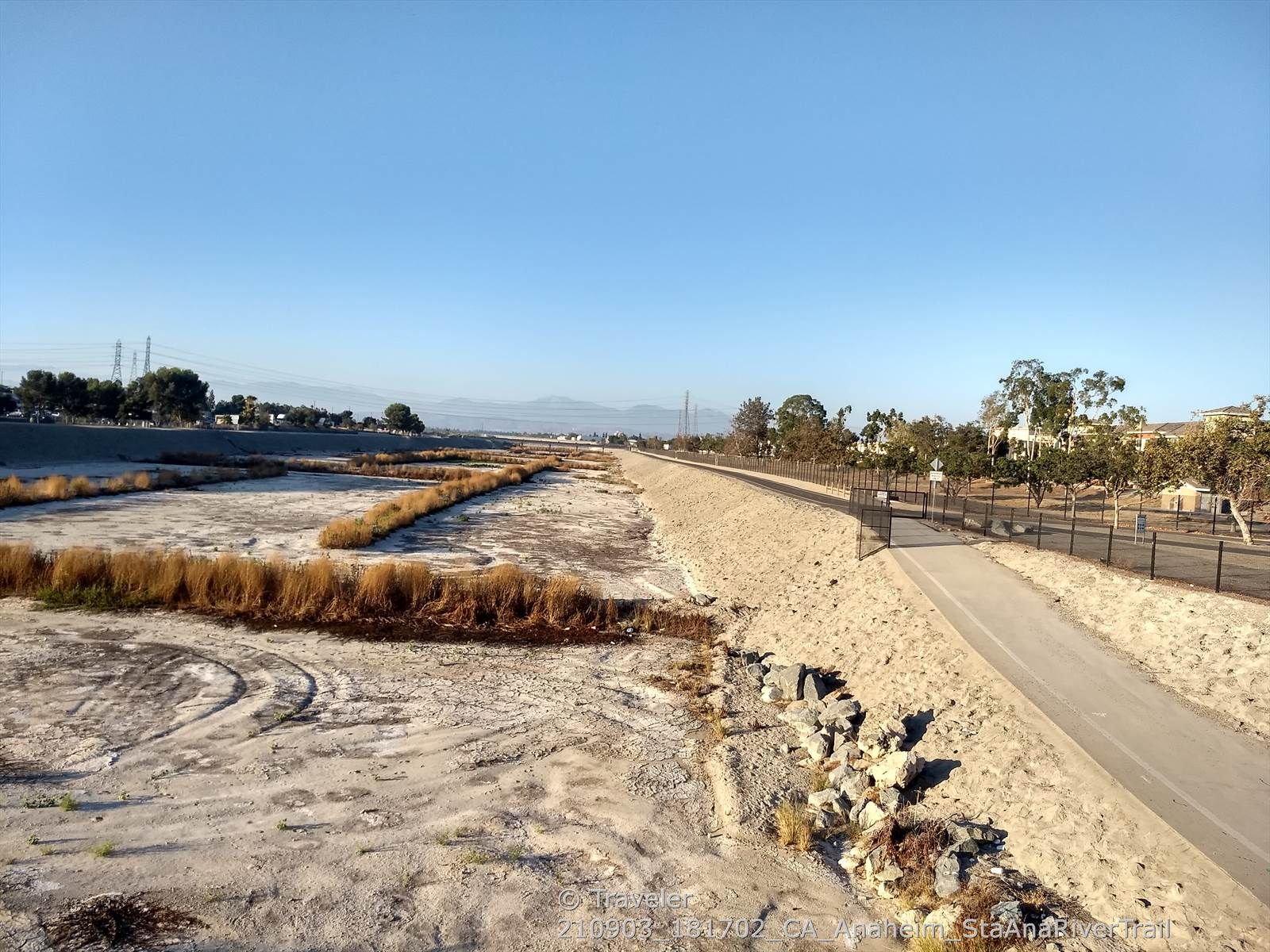 Dry riverbed with vegetation, next to a paved path and fence. - Santa Ana River Trail – Angel Stadium loop from The Outlets at Orange