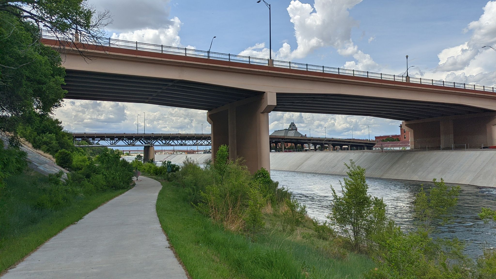 A person walks on a path under highway bridges beside a river. - Pueblo to Beulah loop