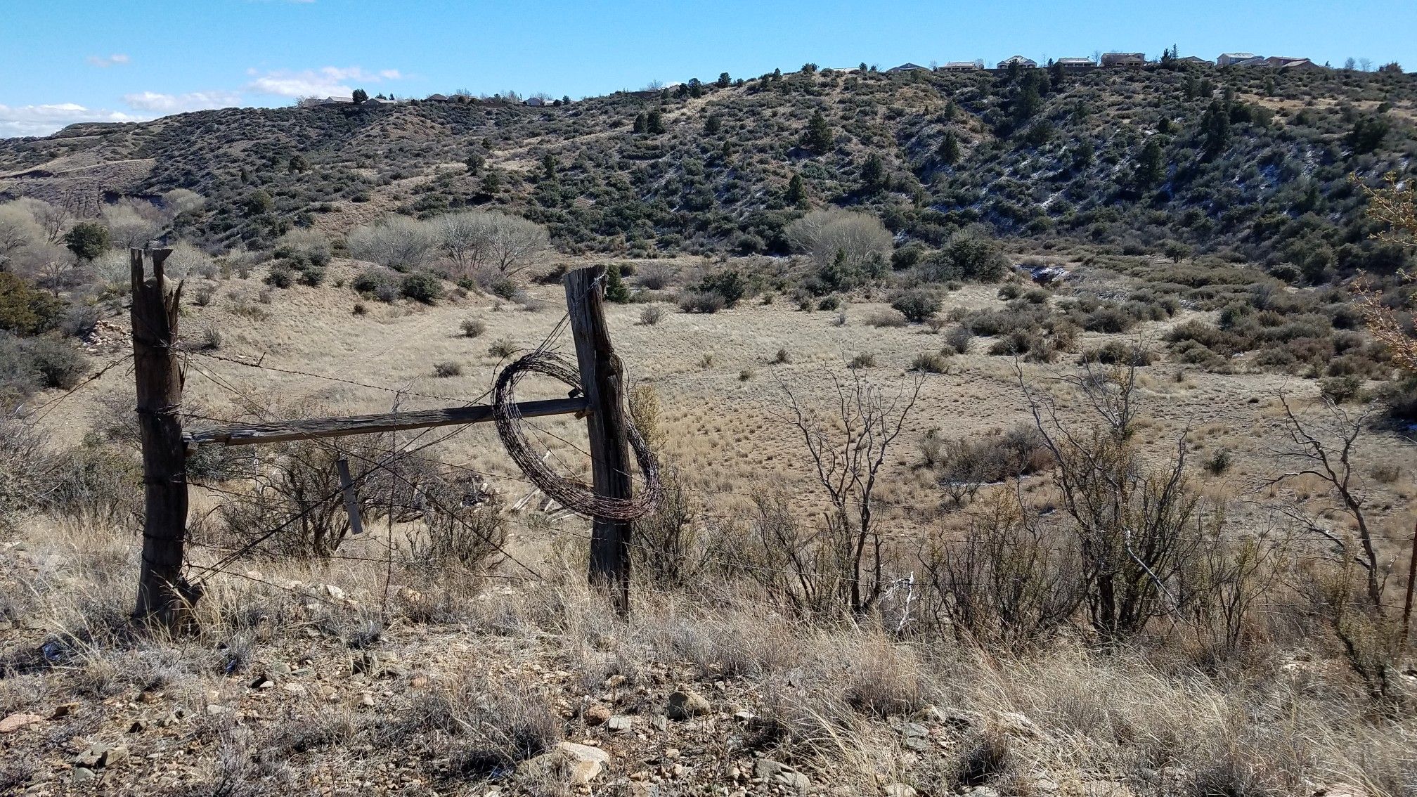 Weathered wooden fence posts in a dry, rocky, hilly landscape under blue sky. - Lynx Creek Loop