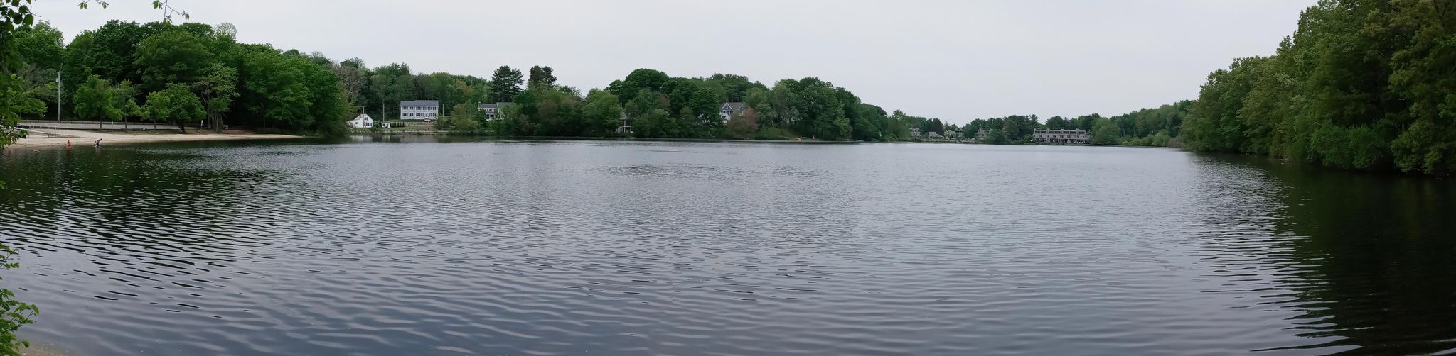 Wide panoramic view of a calm lake surrounded by green trees and distant houses. - Weir Hill Yellow Loop