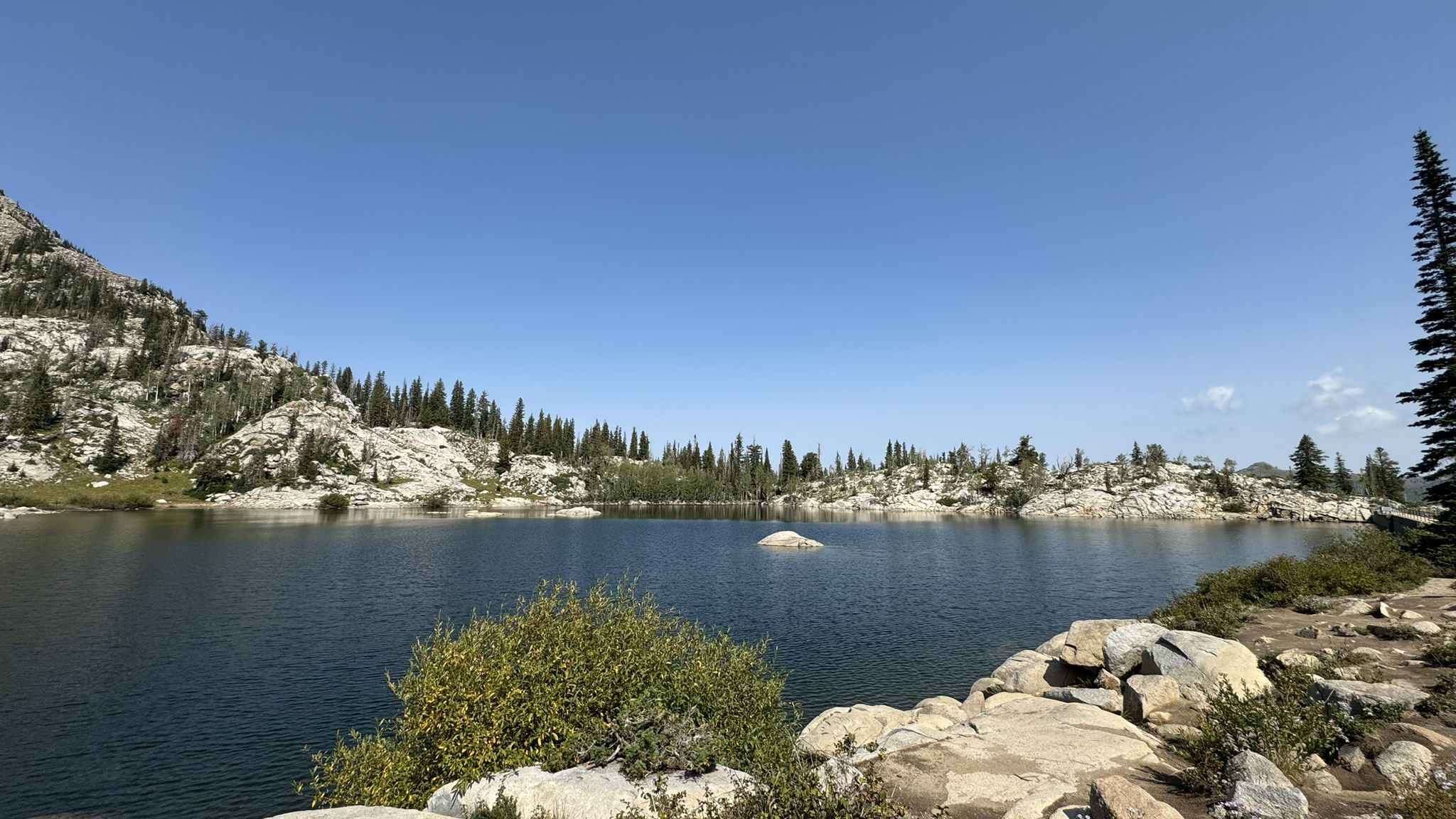 A serene mountain lake with rocky shores and pine trees under a clear blue sky. - Lake Catherine via Brighton Lakes Trail