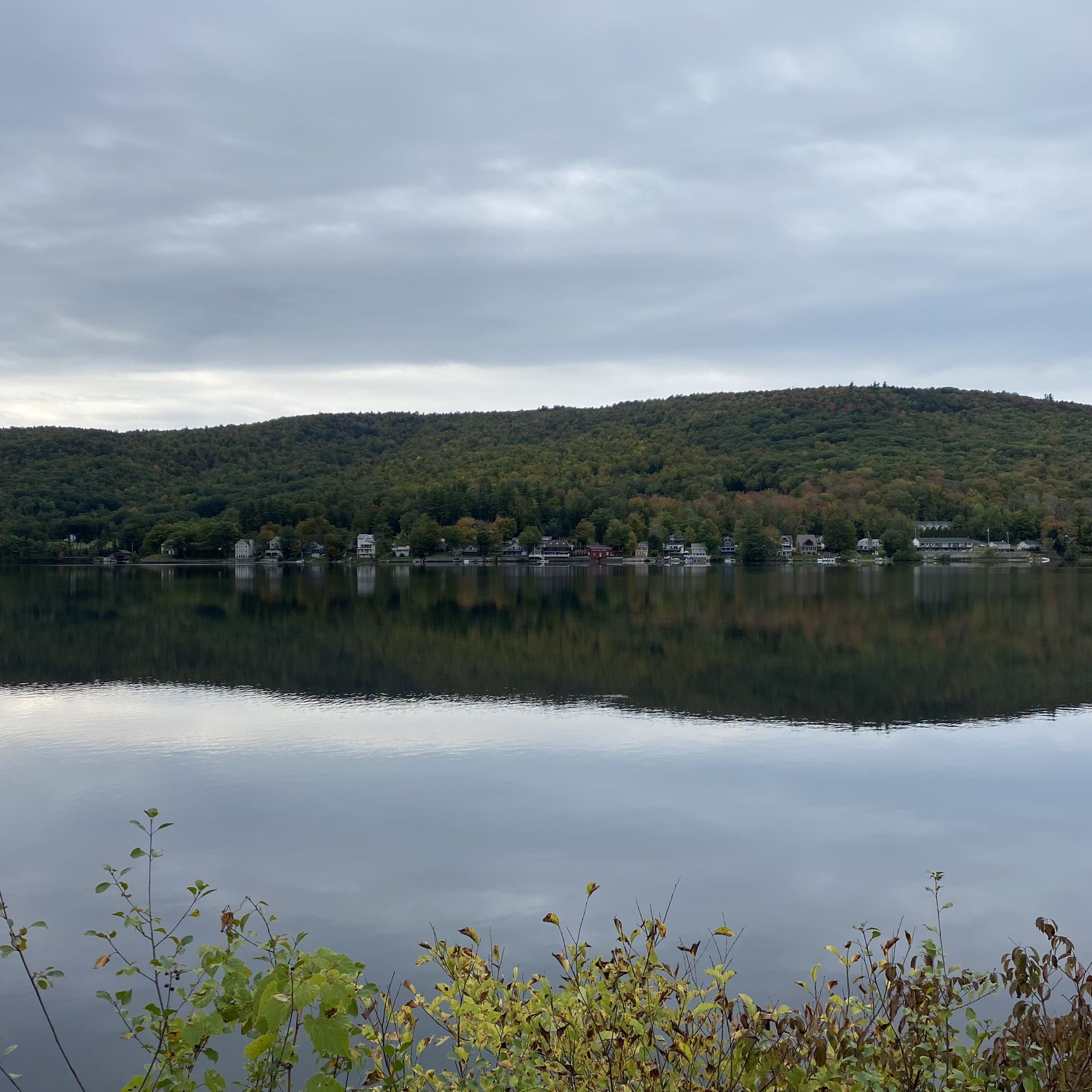Calm lake reflecting cloudy sky and distant forested hills with houses. - Northern Rail Trail – Mascoma Lake loop from Grafton
