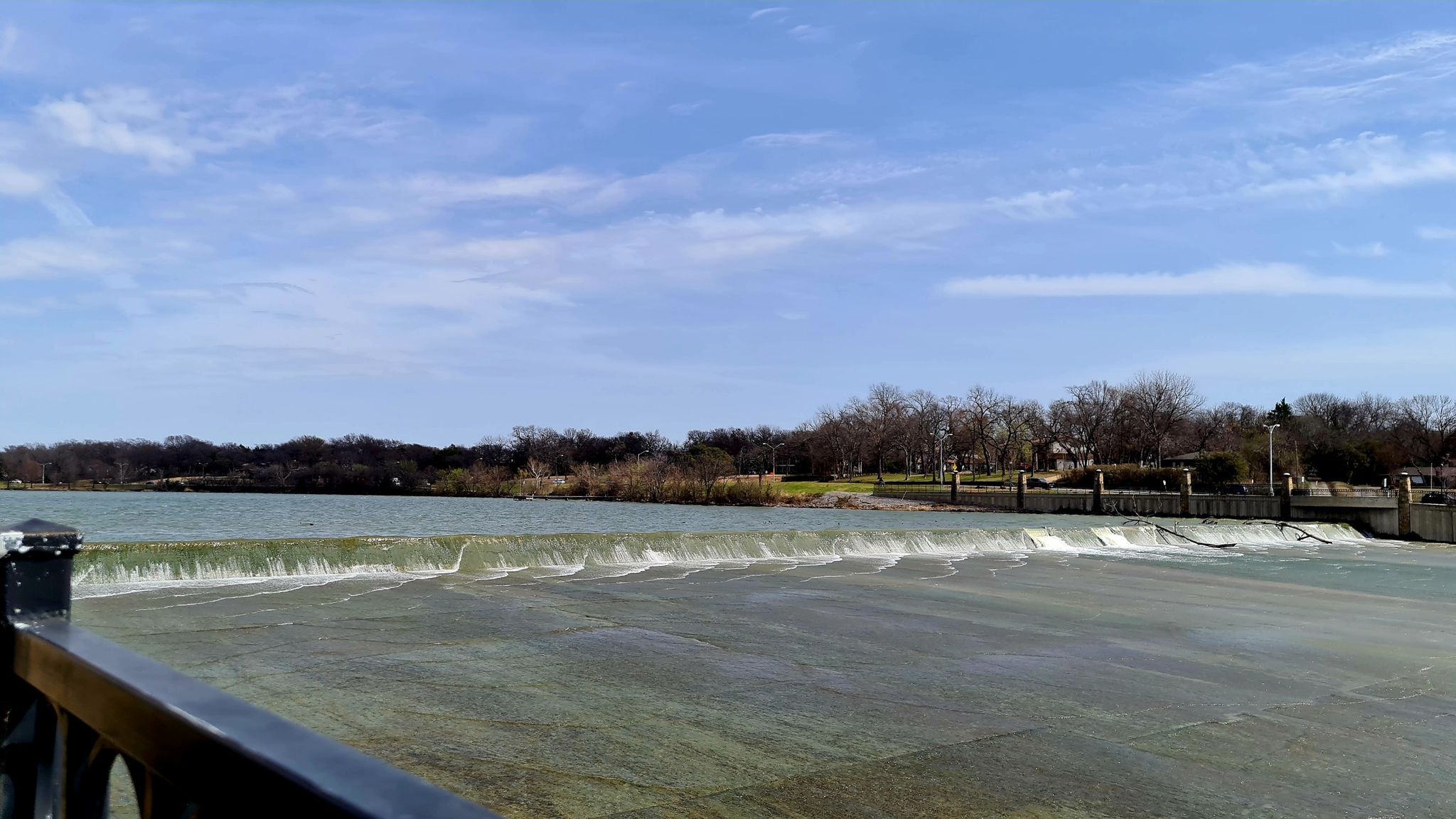 Water flows over a wide dam under a bright blue sky. - White Rock Lake Dam – White Rock Lake Spillway loop from White Rock