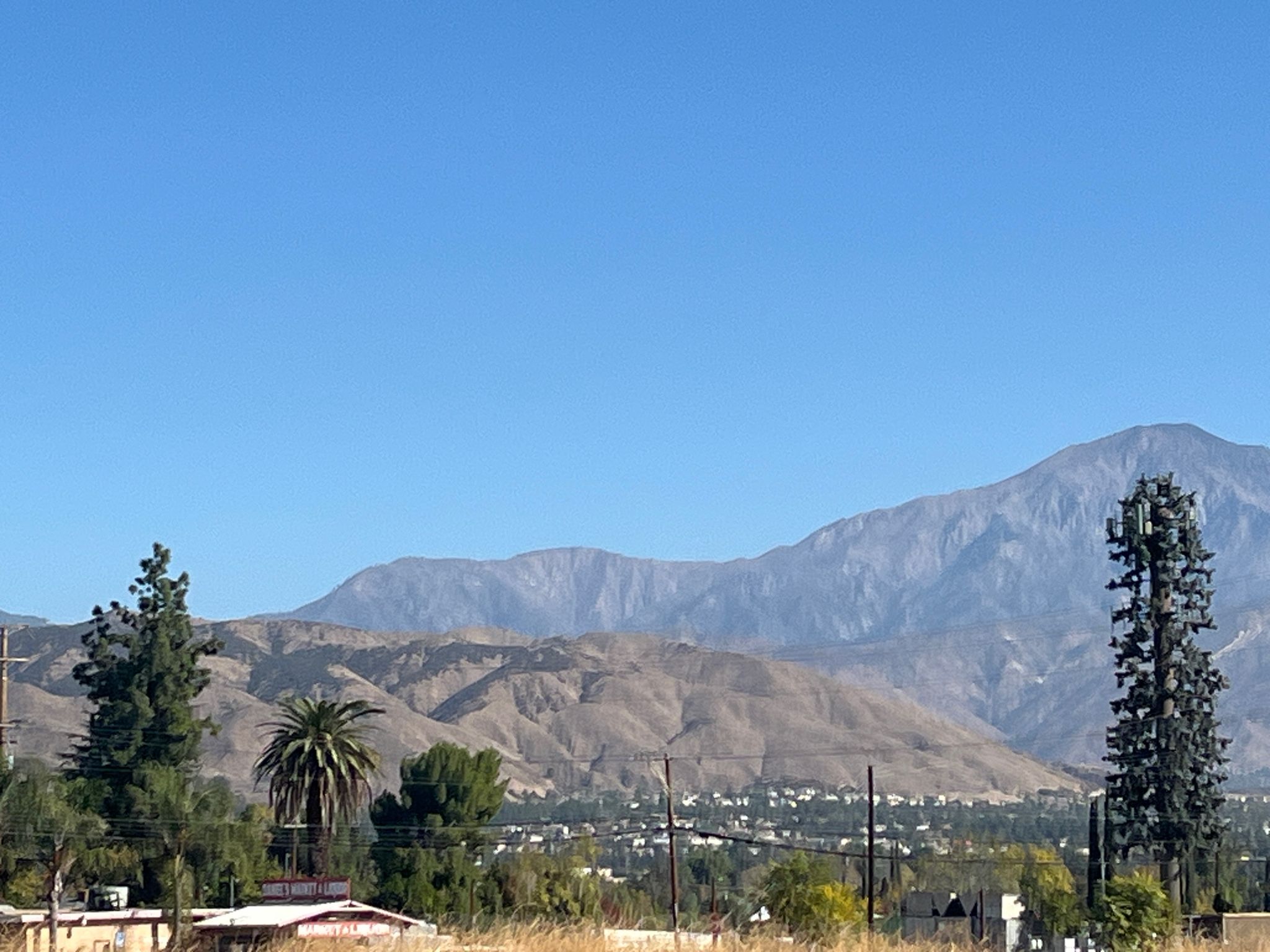Distant mountains overlook a town with a cell tower under a clear sky. - Caroline Park – Three Hawks Trail loop from Loma Linda