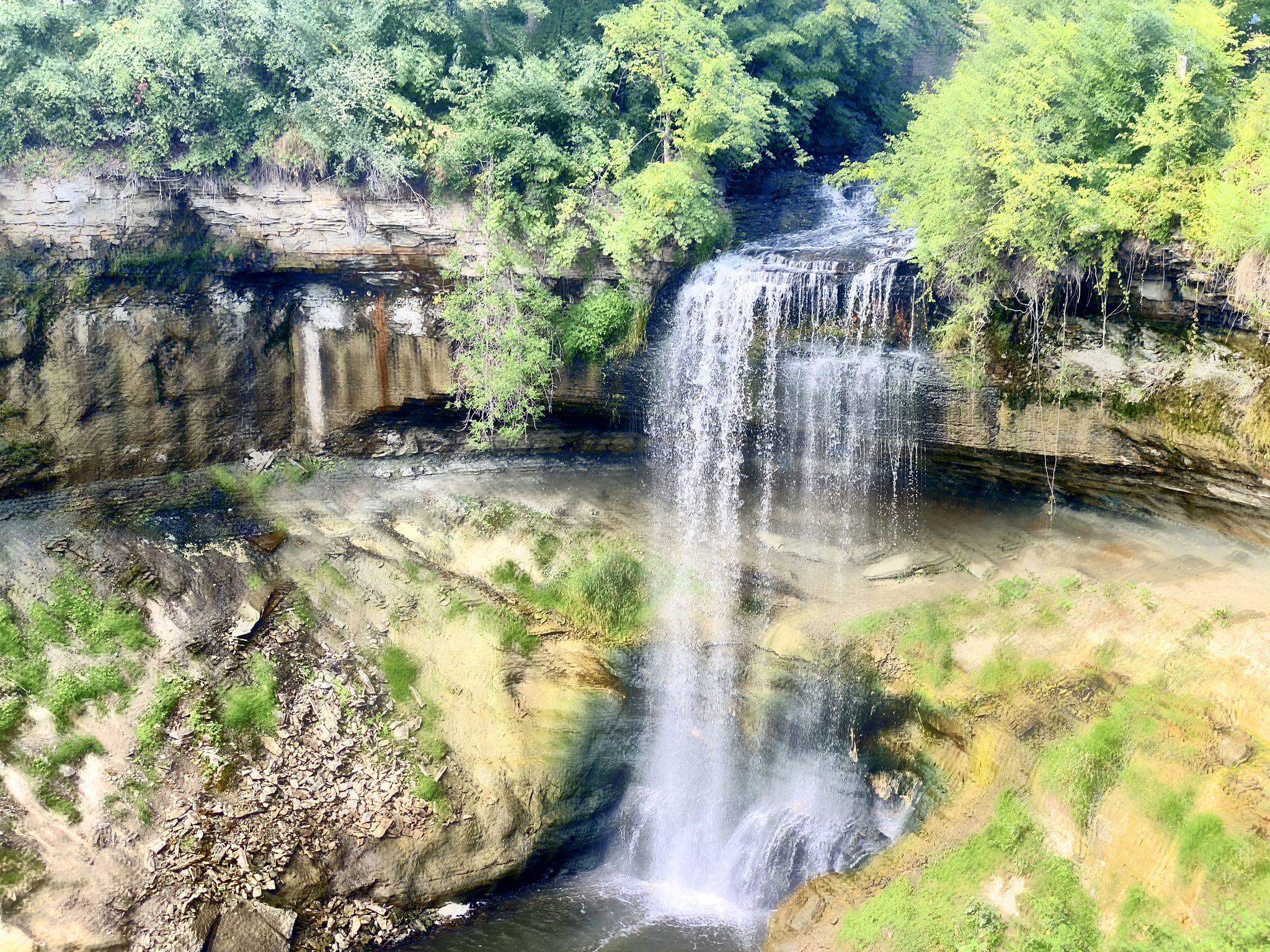 Waterfall plunging over a rocky cliff into a pool, surrounded by green foliage. - Minnehaha Falls – Hiawatha and Minnehaha Statue loop from 50th Street/Minnehaha Park