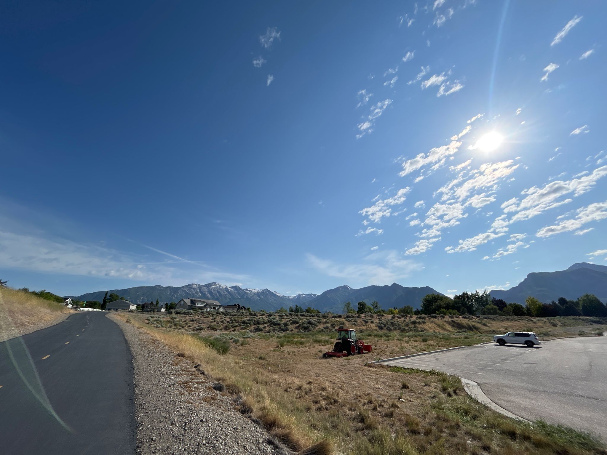 Paved road next to dry fields, distant mountains, and a tractor under bright sun. - Dry Creek Reservoir – Murdock Canal Trail loop from Draper Town Center