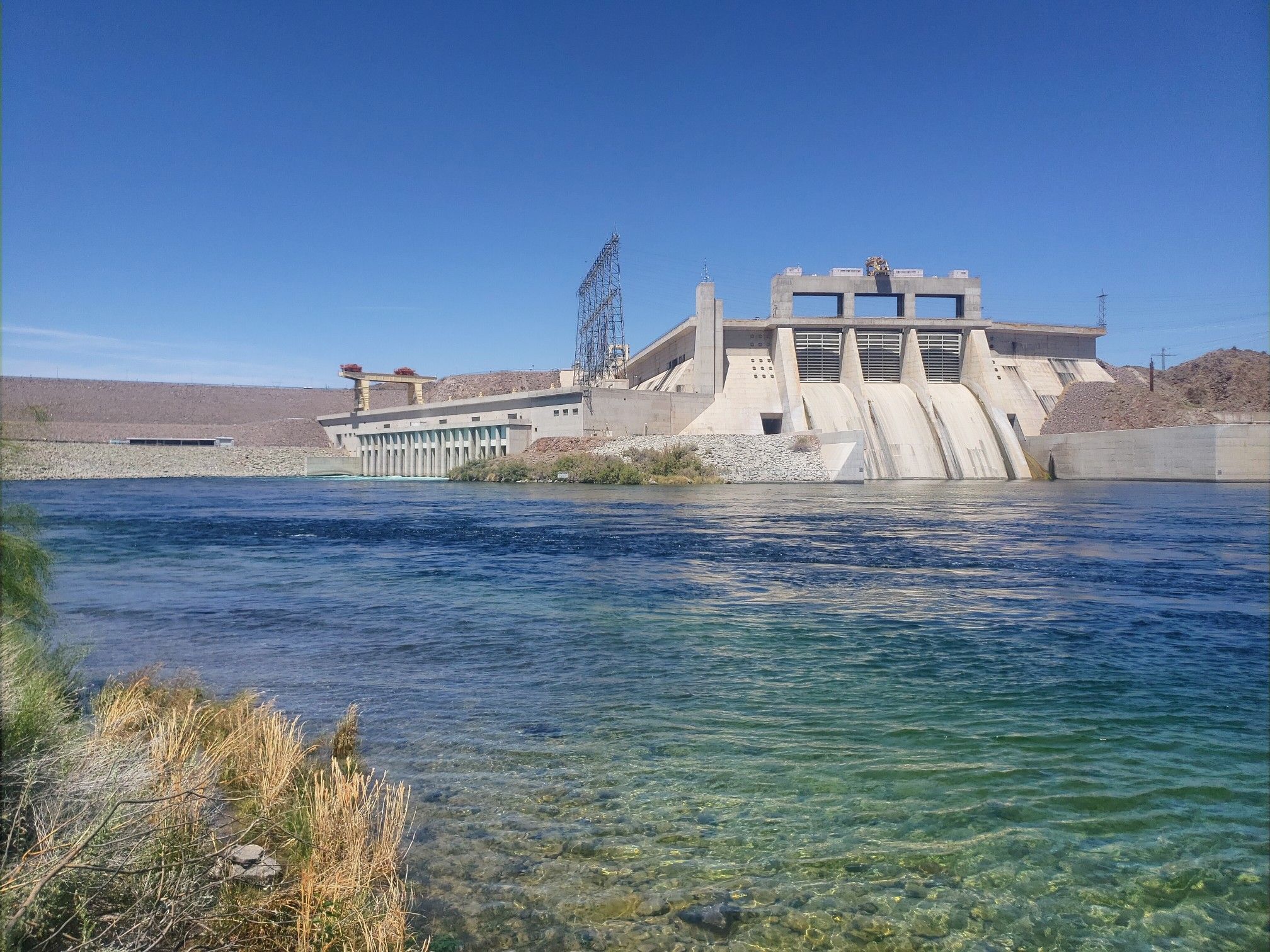 Large concrete dam with spillways under a clear blue sky, wide river in foreground. - Pyramid Canyon Park Loop and Viewpoint