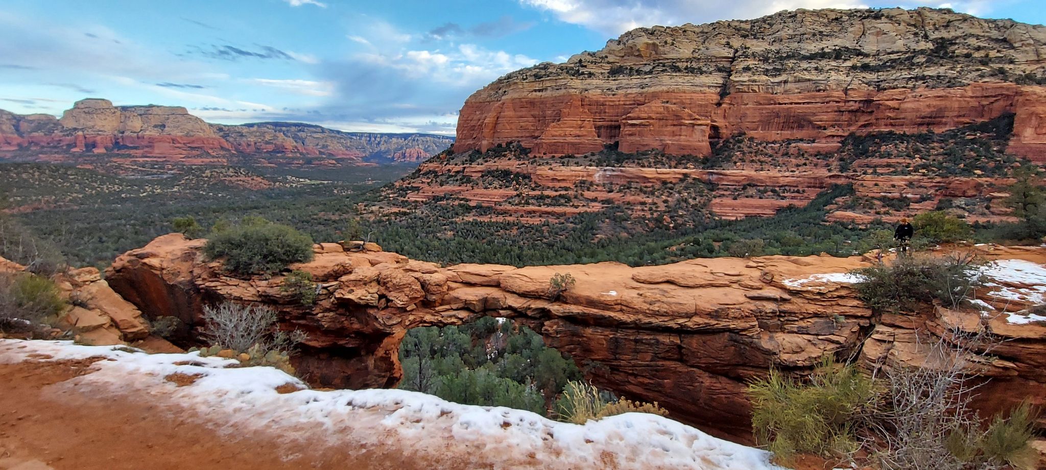 Red rock arch with snow in the foreground, overlooking a green valley. - Devil's Bridge Trail via Dry Creek Road