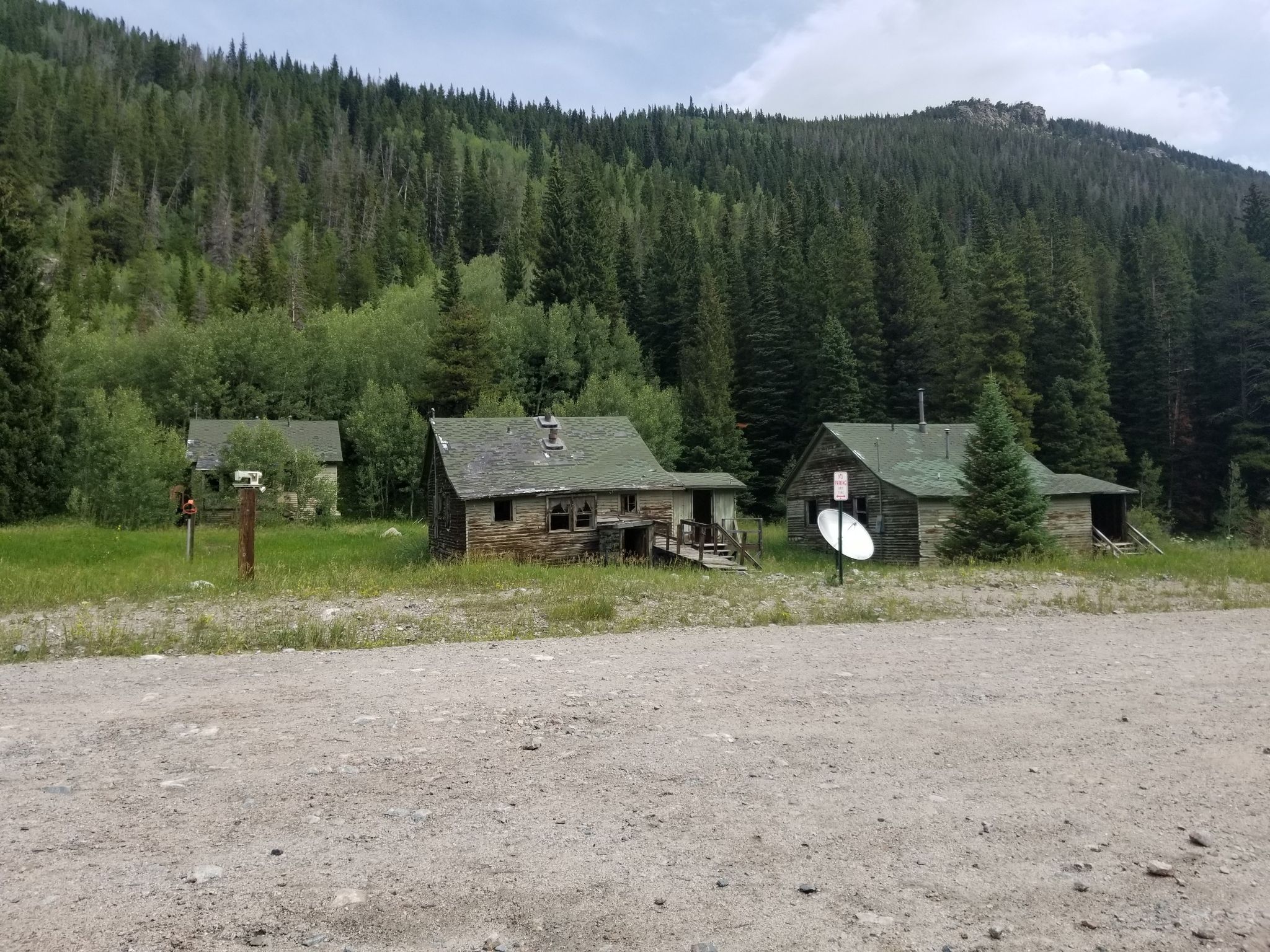 Three rustic cabins in a grassy clearing, backed by a dense evergreen forest. - Public toilet in Rollinsville – Tolland loop from Rollinsville