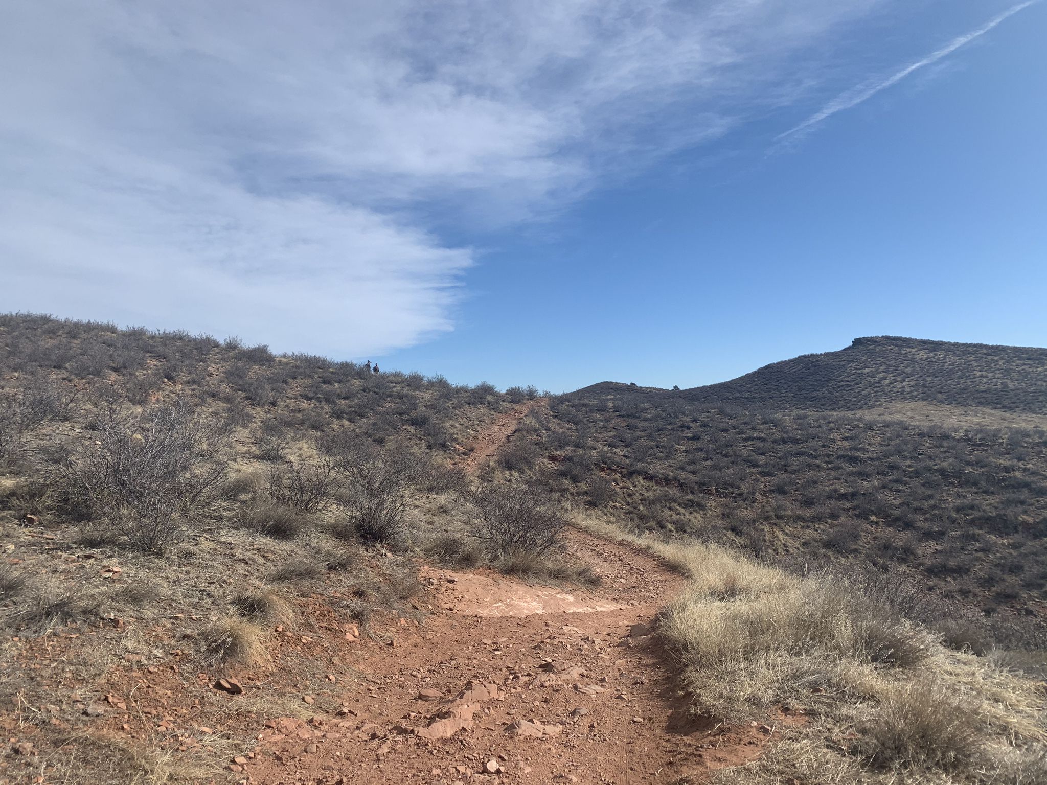 Red dirt trail ascending a dry, brush-covered hill under a clear blue sky. - Devil's Backbone Trailhead – Devils Backbone Open Space loop from Morey Wildlife Reserve