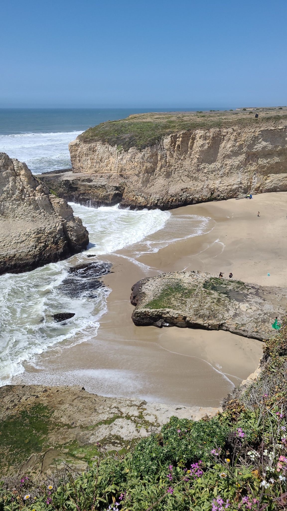 Sunny aerial view of a sandy cove with crashing waves and rugged cliffs. - Shark Fin Cove Loop