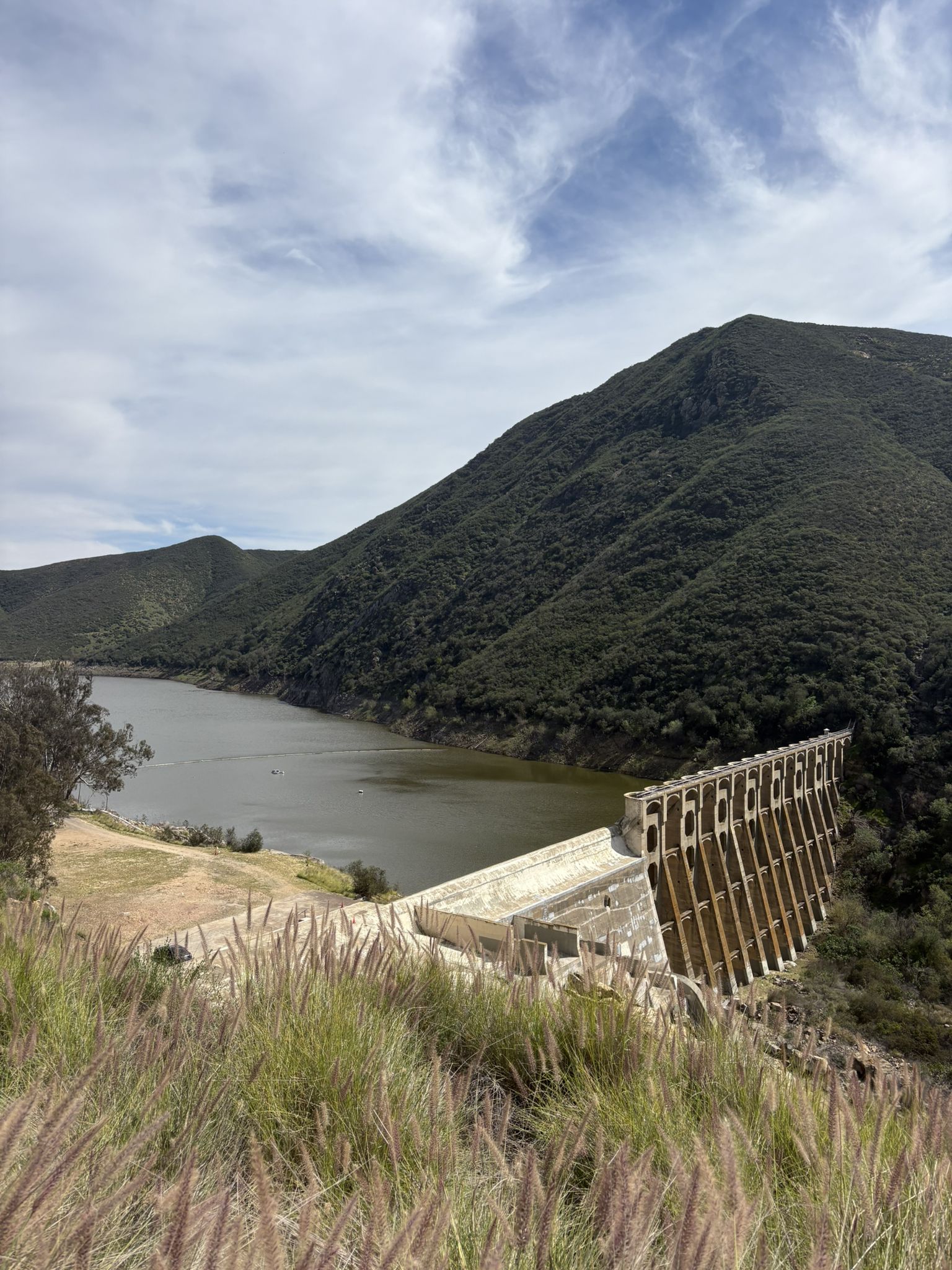 Partly cloudy view of a dam and reservoir nestled between steep green hills. - Moonlight Beach Overlook – San Elijo Road Climb loop from Encinitas Station