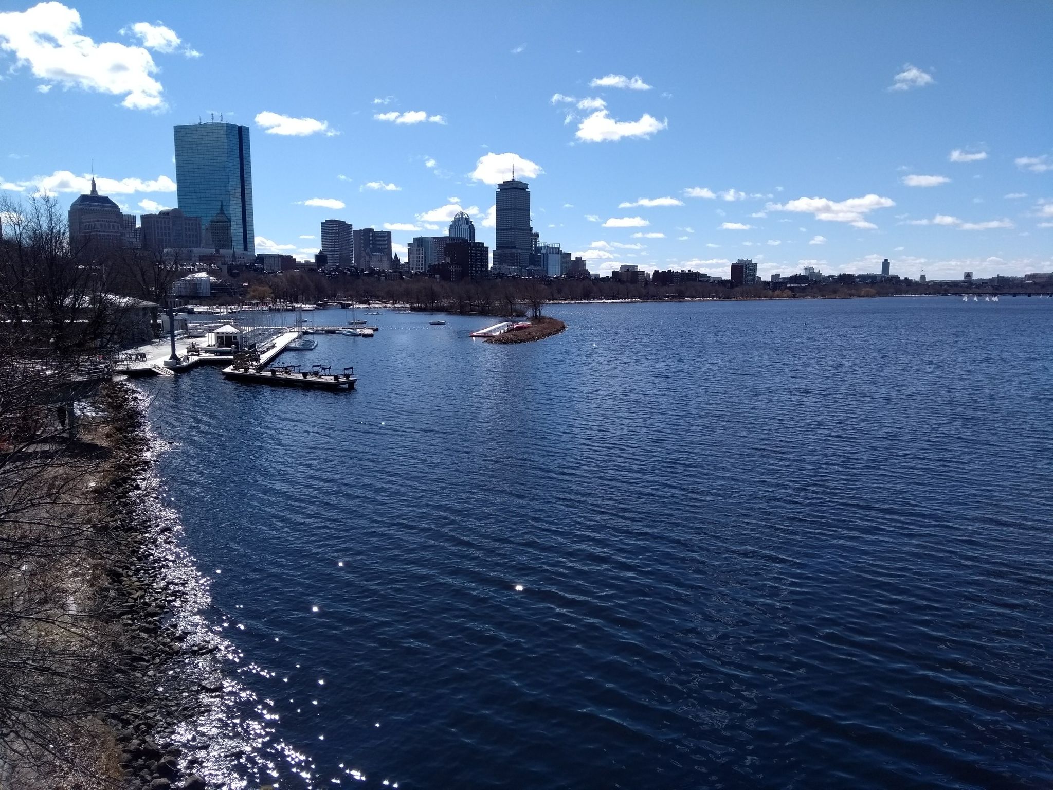 A wide river with docks and a distant city skyline under a bright blue sky with clouds. - Longfellow Bridge – Acorn Street loop from Kendall/MIT