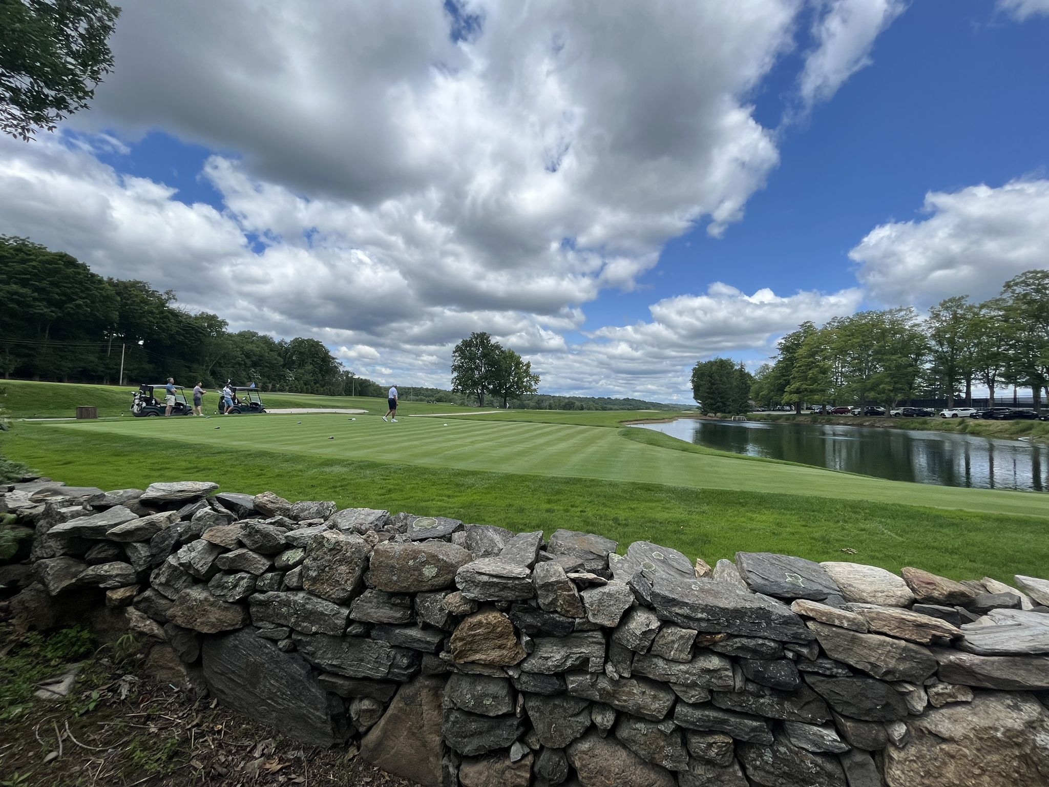 Stone wall overlooking a golf course with distant golfers and a pond. - View of the Long Island Sound – Byram River Marina loop from Harrison