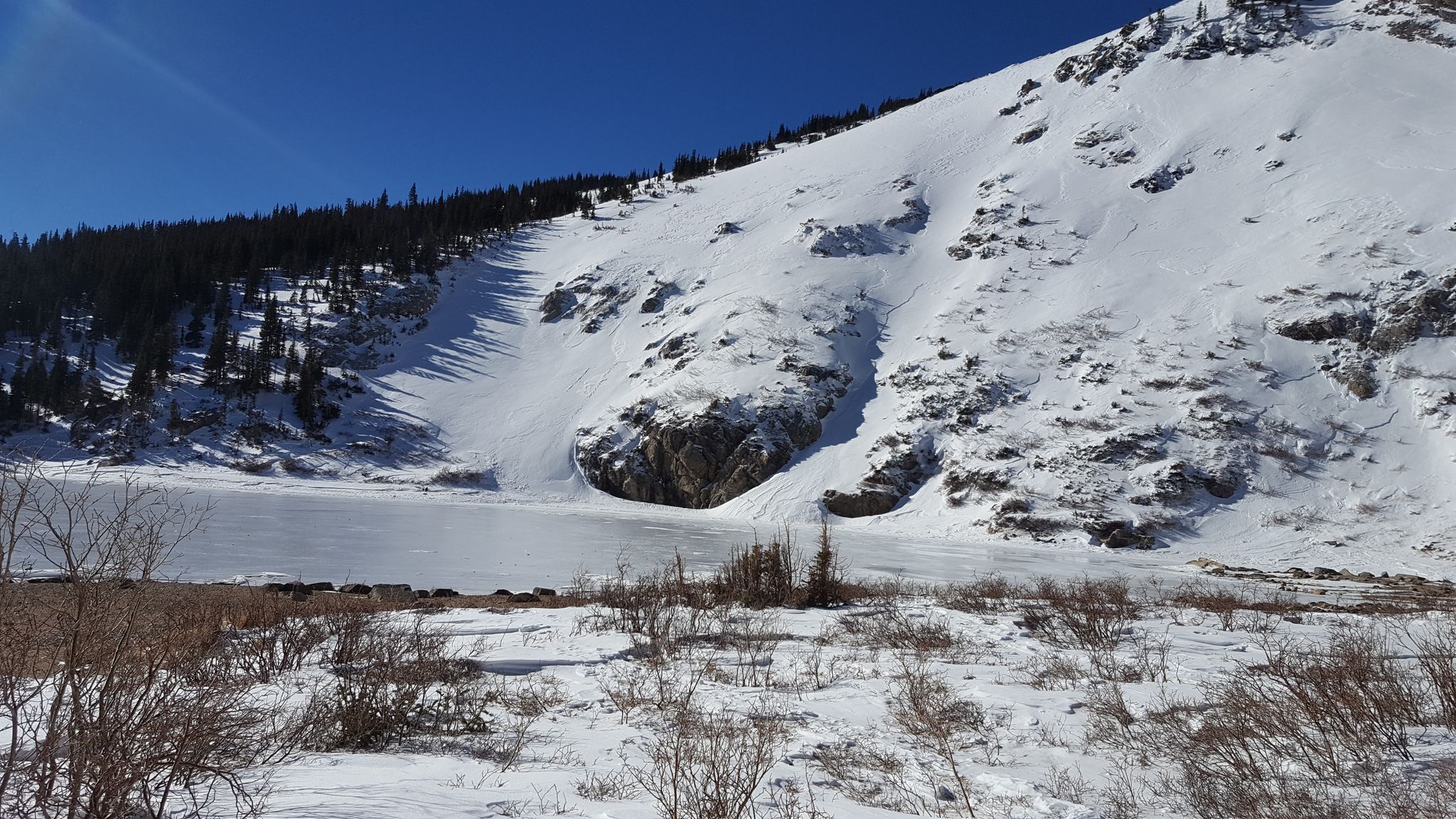 Frozen lake at the base of a snow-covered mountain, clear blue sky. - Kingston Spur East via St. Mary's Glacier
