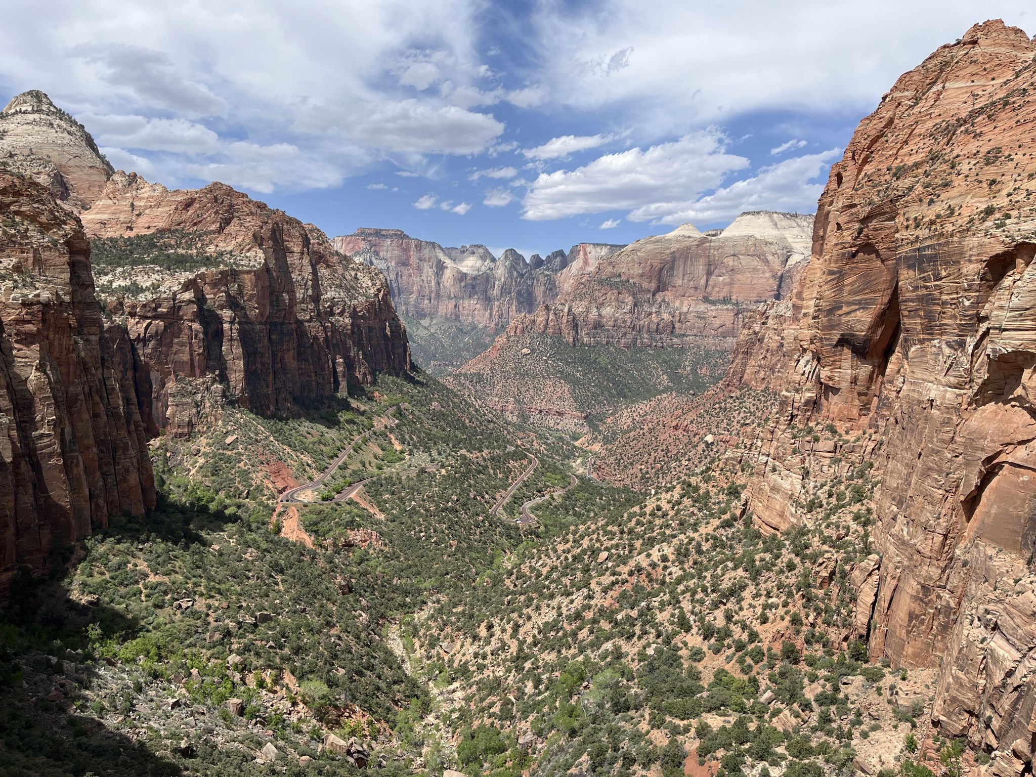 Wide view of a vast canyon with towering red rock cliffs under a cloudy sky. - Canyon Overlook Trail
