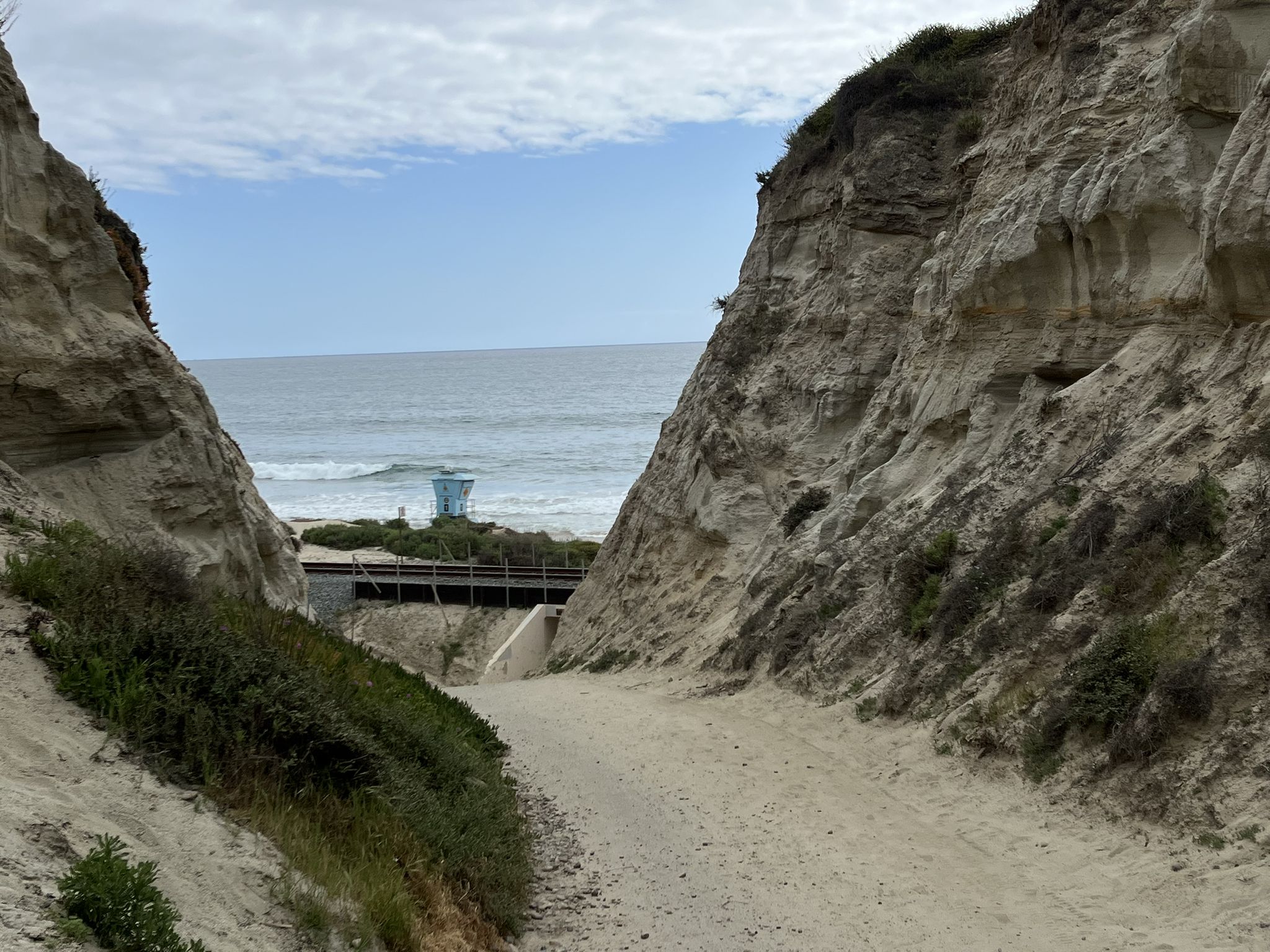 Sandy path between cliffs leading to the ocean and a distant lifeguard tower. - San Clemente Beach Trail