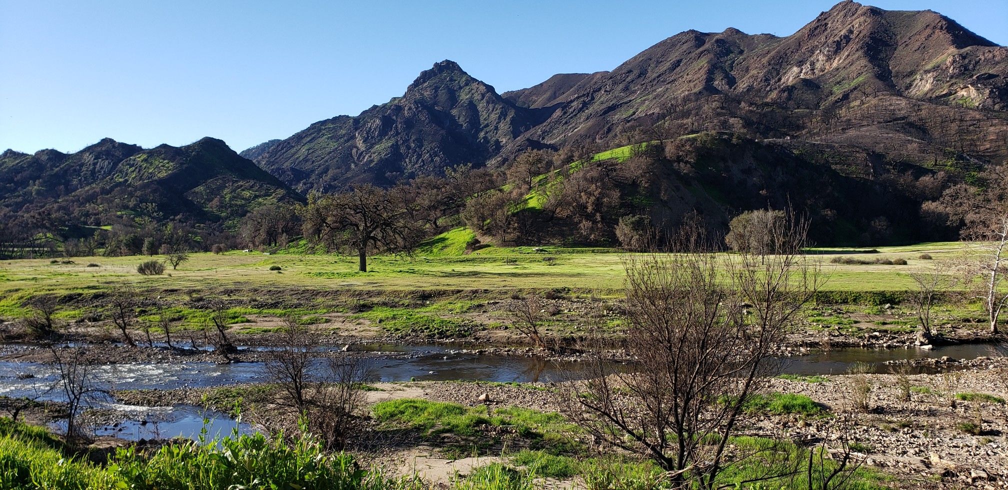 River flowing through a green valley with mountains under a clear sky. - Malibu Creek State Park loop