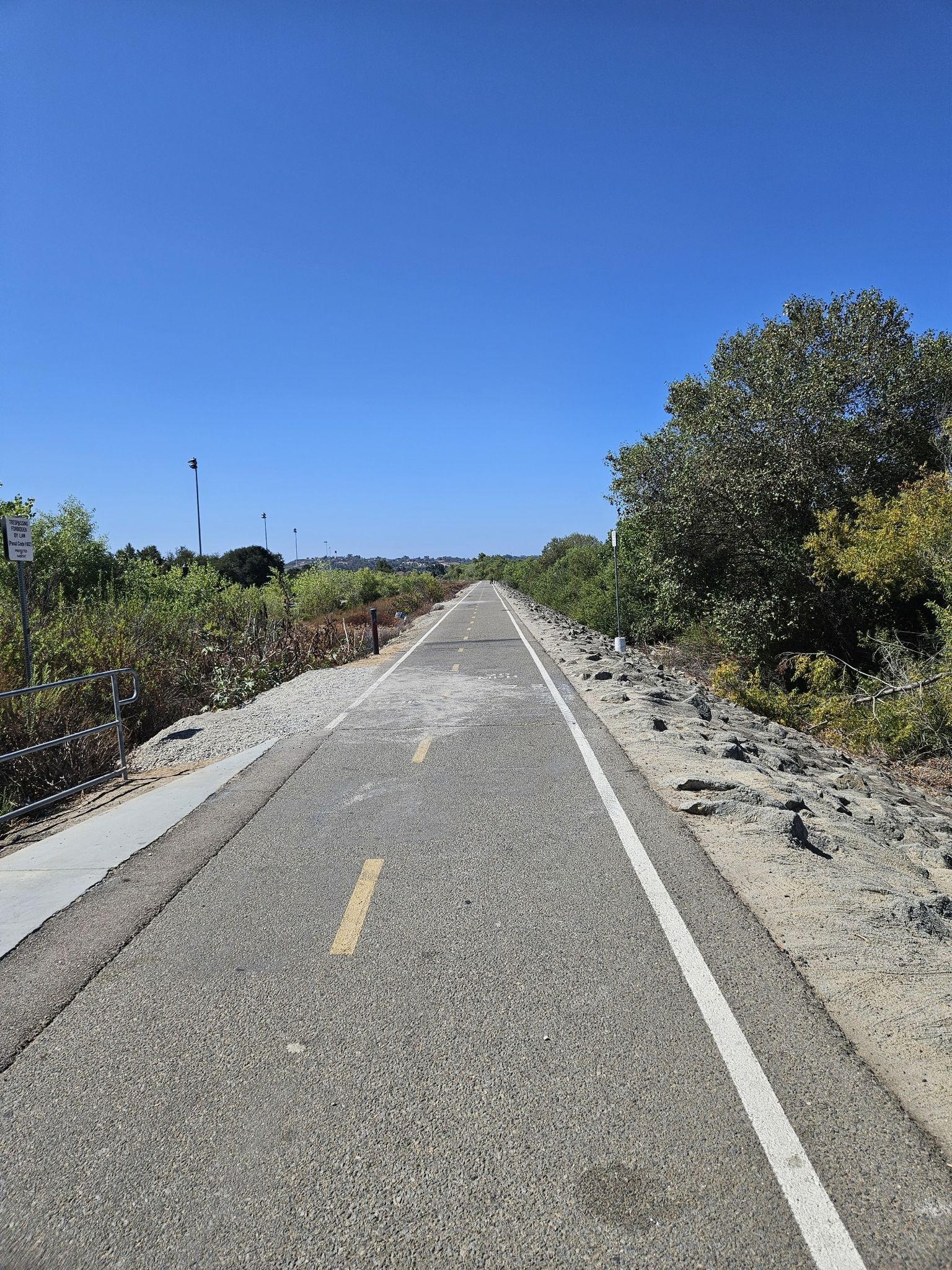Long, straight paved path bordered by trees under a clear blue sky. - Mance Buchanon Park – San Luis Rey Bike Path loop from Victoria's