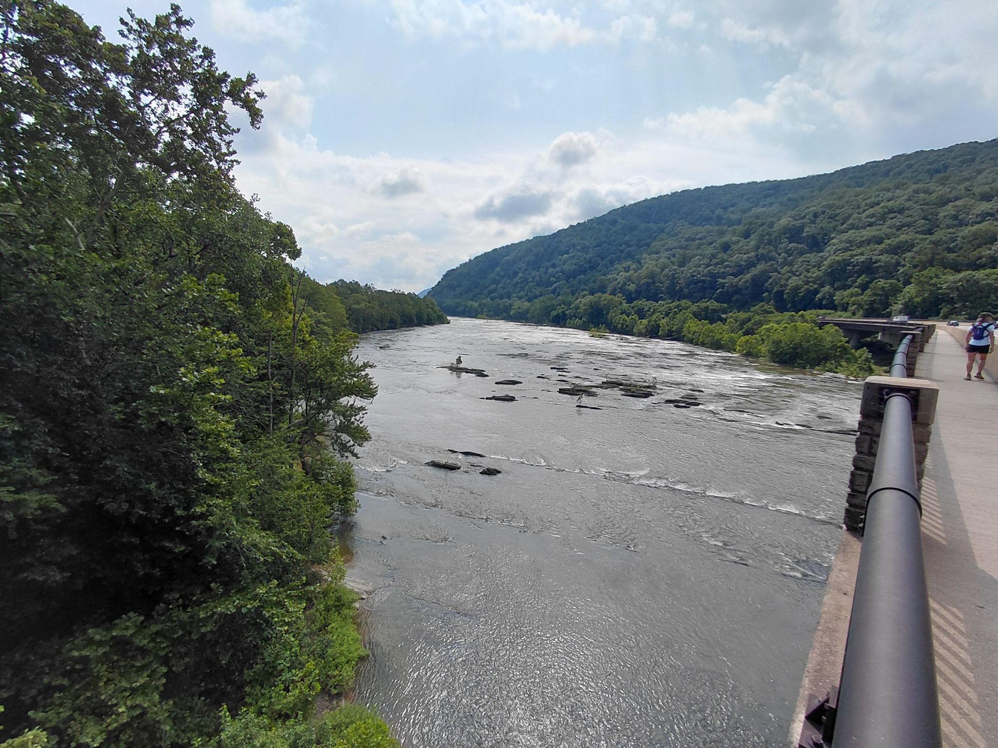 Wide river with a paddleboarder, flanked by forested hills under a cloudy sky. - Loudoun Heights Trail to Split Rock