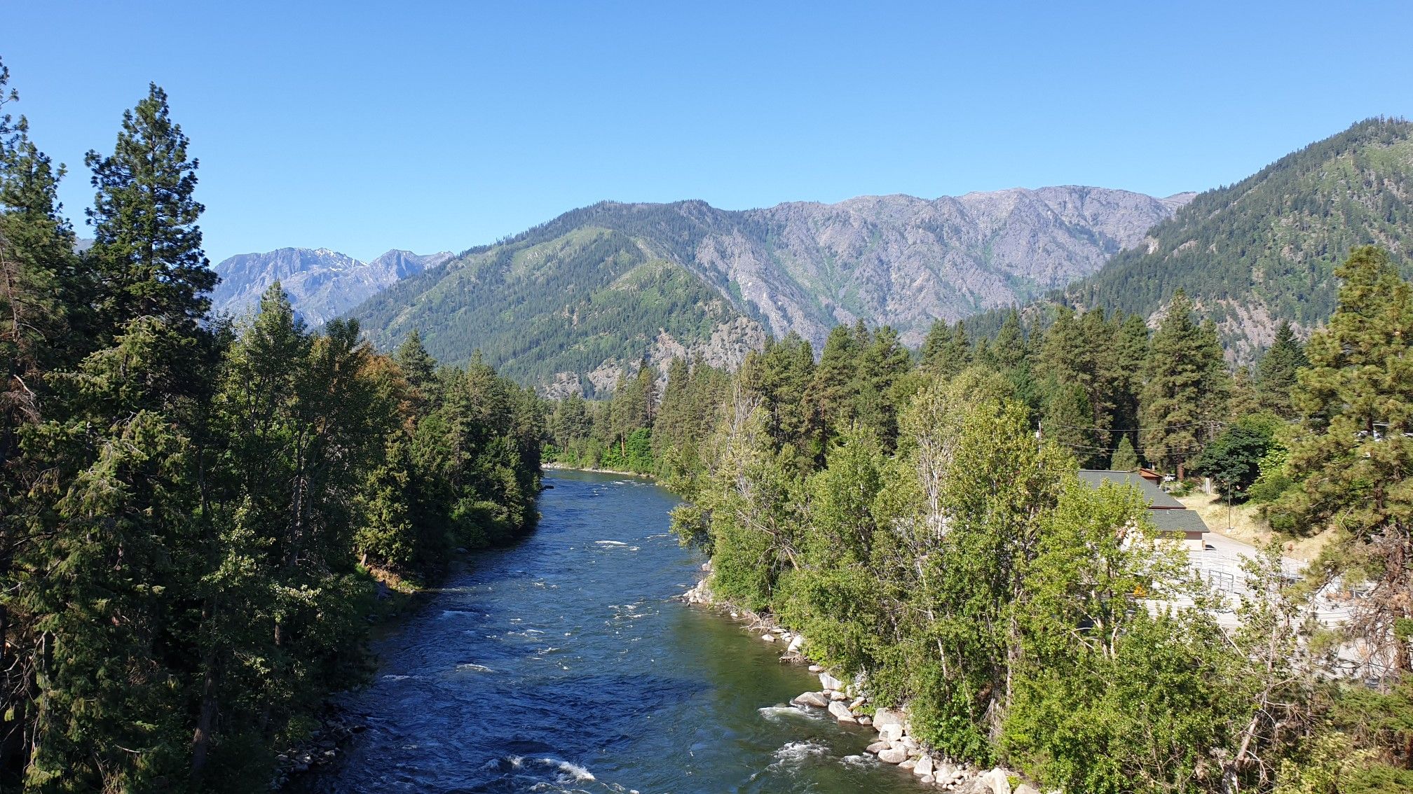 A wide river flows through a green forested valley under a clear blue sky. - Leavenworth loop via East Leavenworth Road & Icicle Road