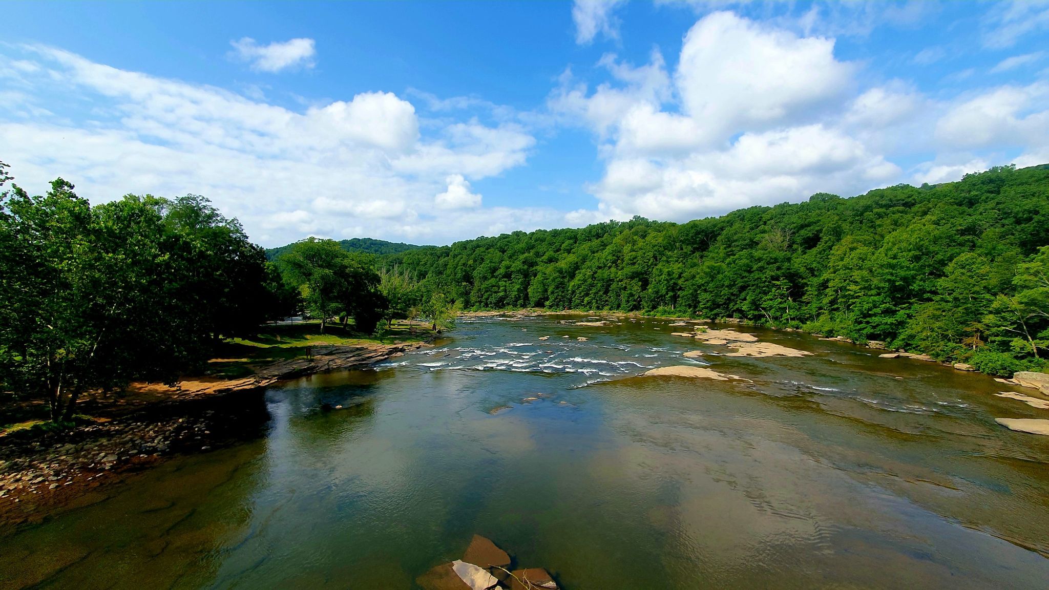 A wide river with rapids flows through a green forested landscape under blue sky. - Ohiopyle – Ohiopyle State Park loop from Ohiopyle State Park