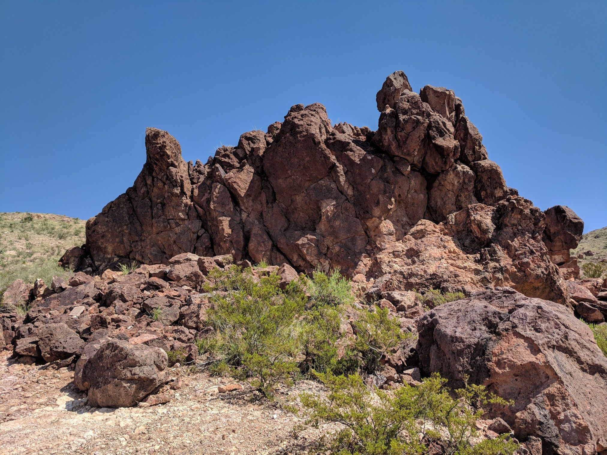 Jagged brown rock formations and sparse green bushes under a clear blue sky. - Picacho Peak Via Box Canyon Loop Trail