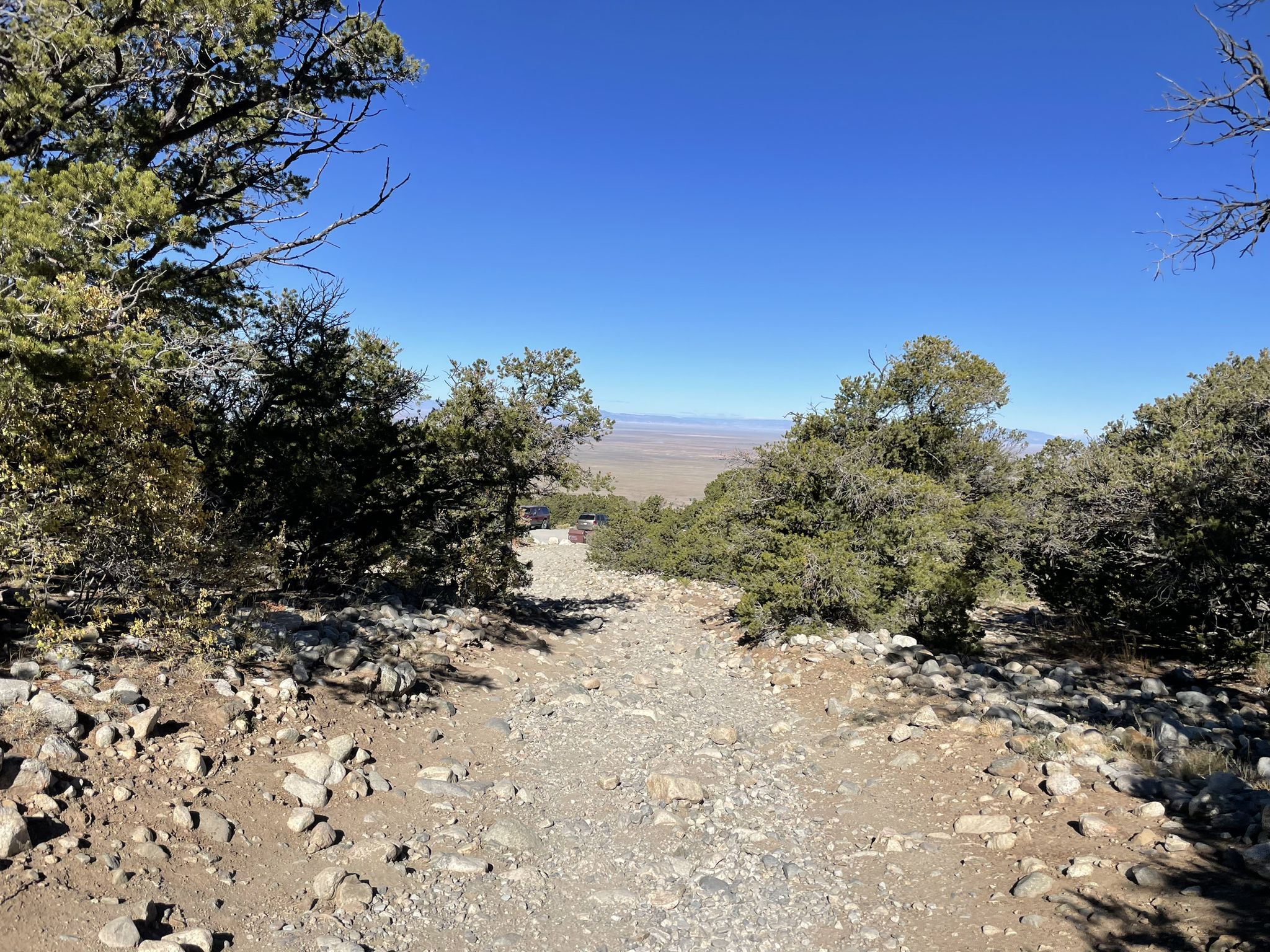 Rocky dirt path descends through sparse trees with a distant plain visible. - Zapata Creek and benches – Zapata Falls loop from Zapata Falls