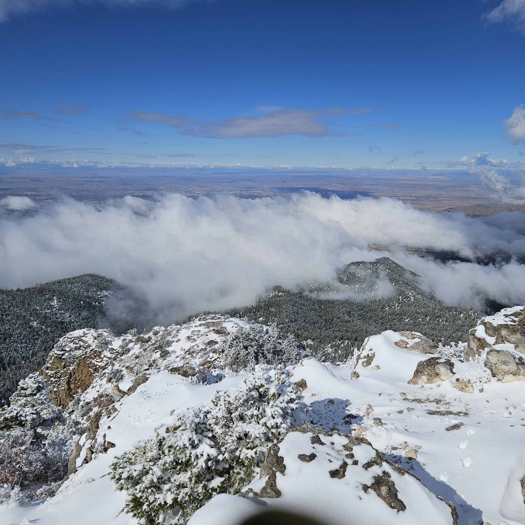 Snowy mountain peaks overlook a vast cloud-filled valley on a bright day. - South Sandia Peak via South Crest and CCC Trail Loop