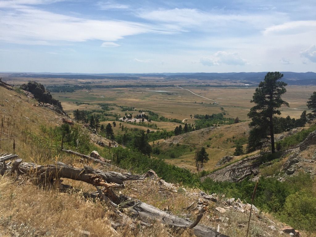 Wide valley view with hills, scattered trees, and distant plains under a cloudy sky. - Bear Butte