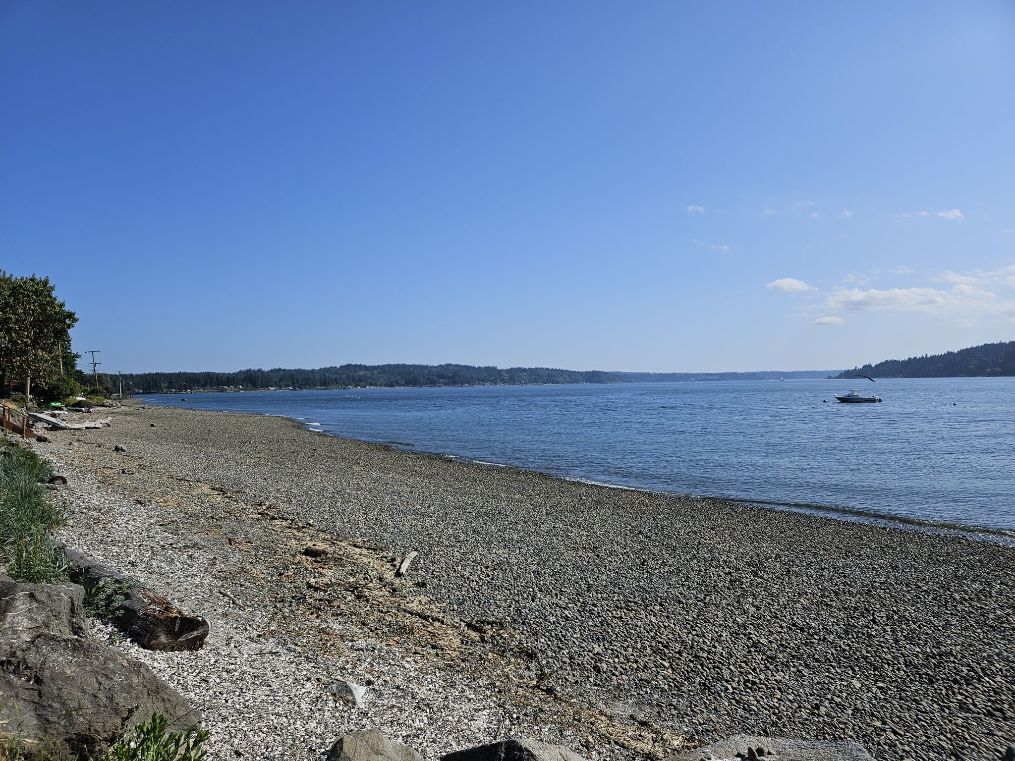 Wide pebbly beach next to calm blue water, with a distant boat. - Veterane Open Space Trail loop from Illahee State Park