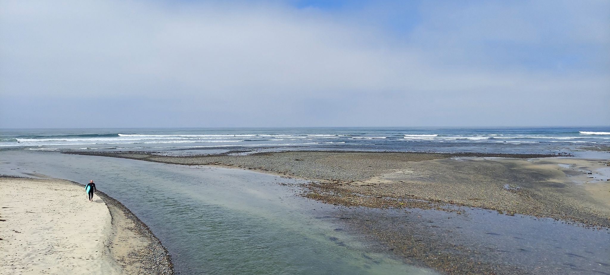 River flowing into the ocean, with a person carrying a surfboard. - San Elijo Lagoon Estuary Canal – Swami's Seaside Park loop from Hunter 1940 Parking Lot