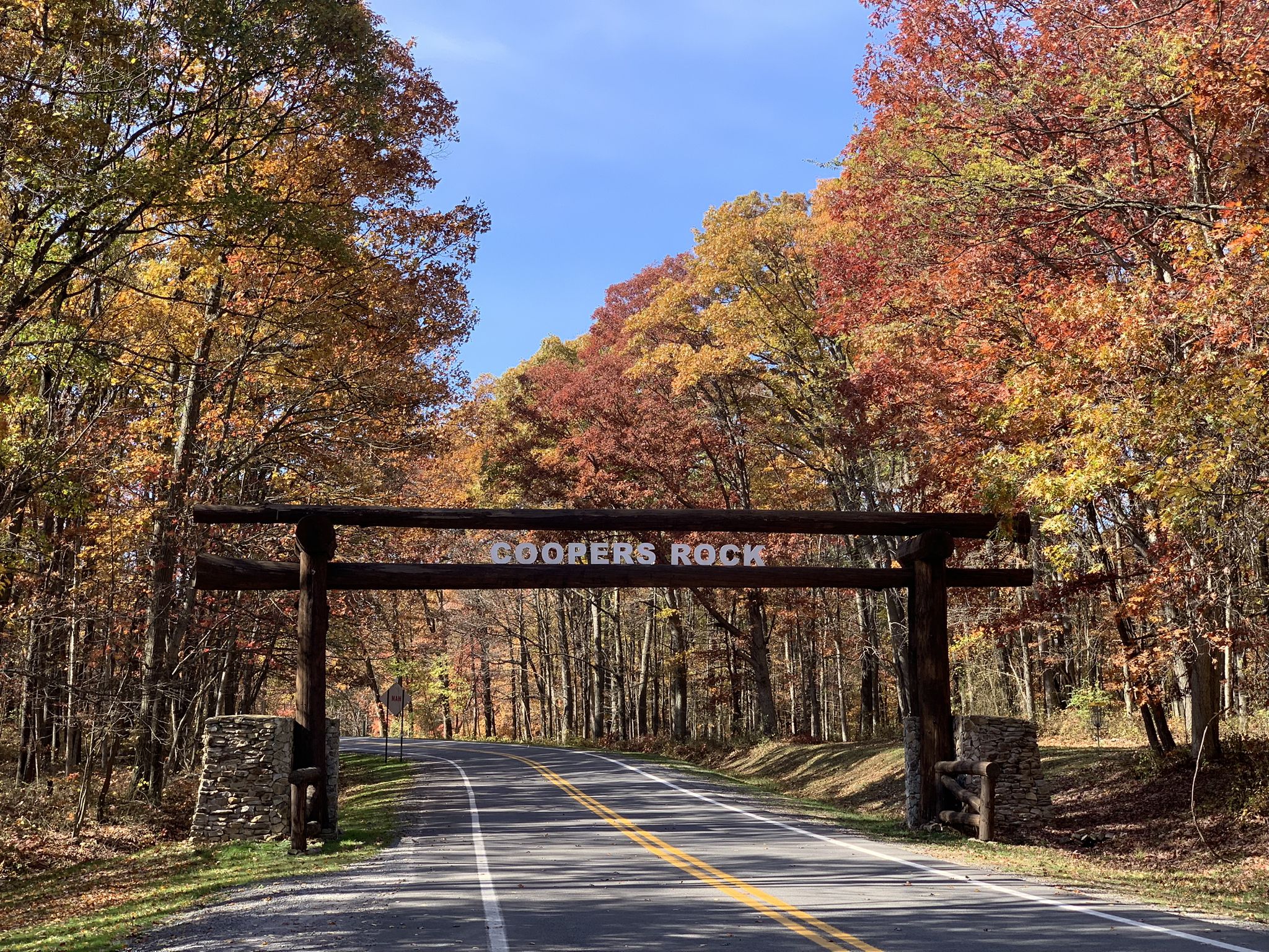 Wooden archway over a sunlit road lined with vibrant autumn trees. - Morgantown to Coopers Rock State Forest