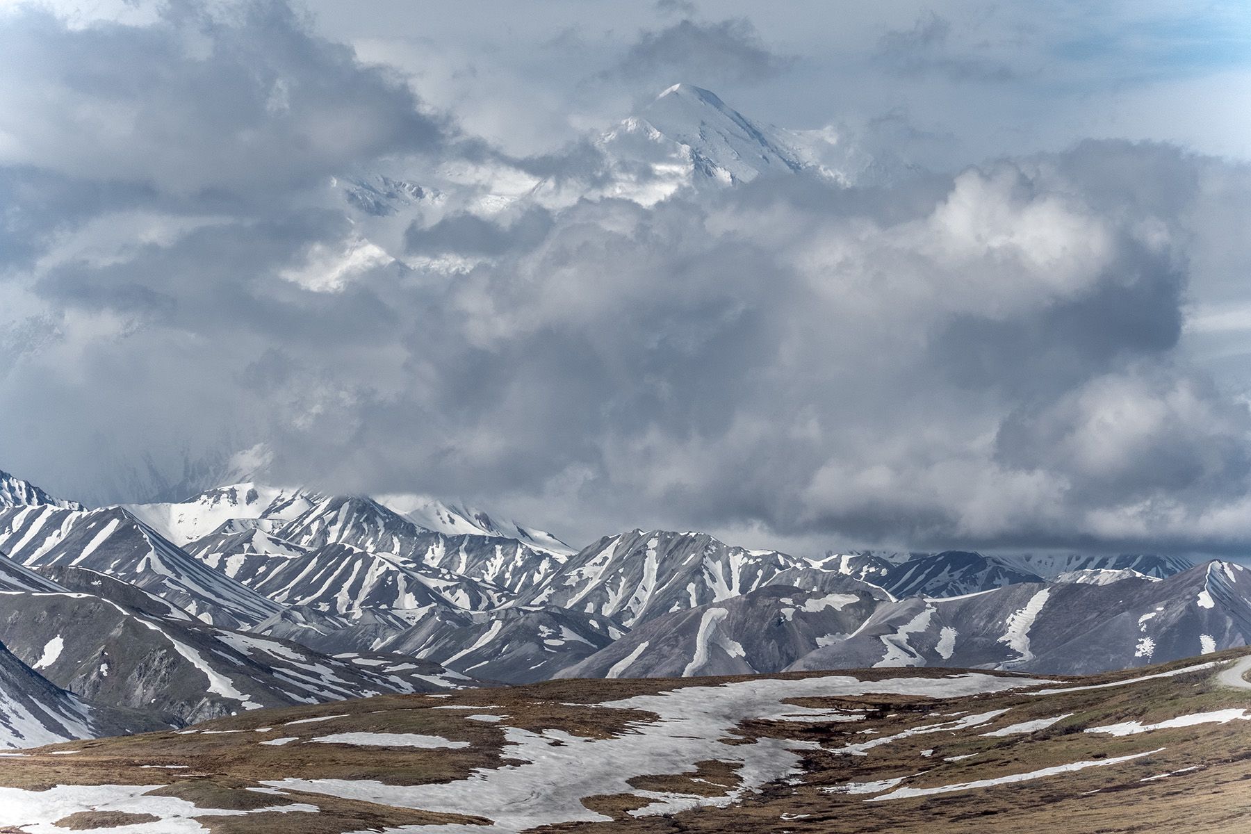 Distant snow-capped mountain peaks shrouded in clouds over a rugged landscape. - Eielson Alpine Trail