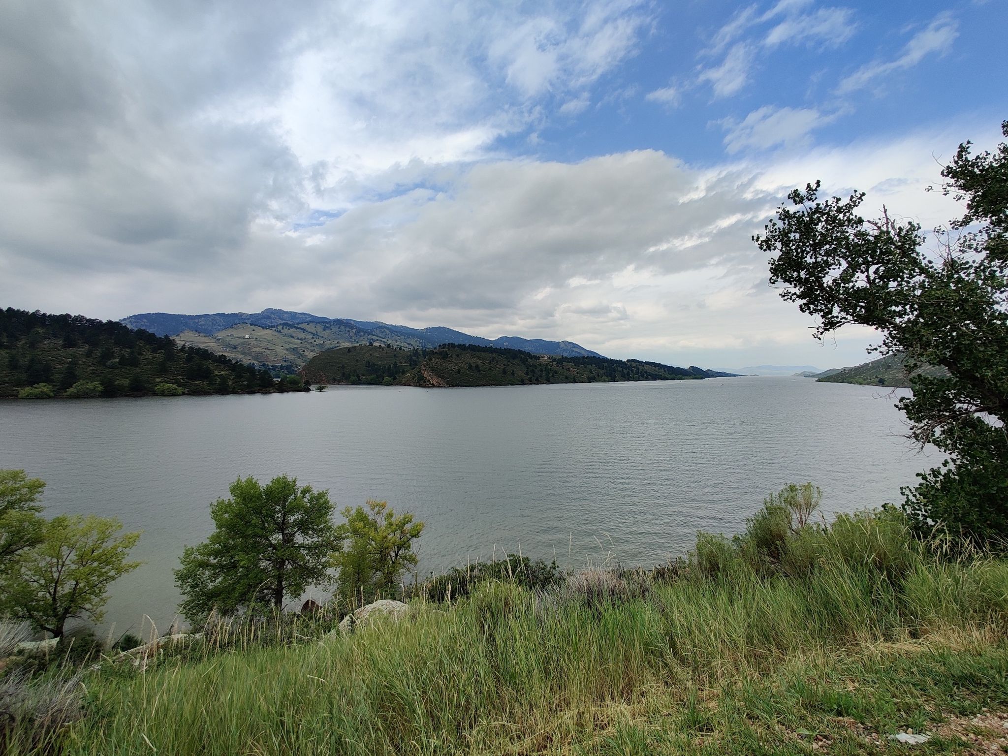 Wide lake surrounded by green hills under a cloudy sky. - Horsetooth Falls and Rock Trail