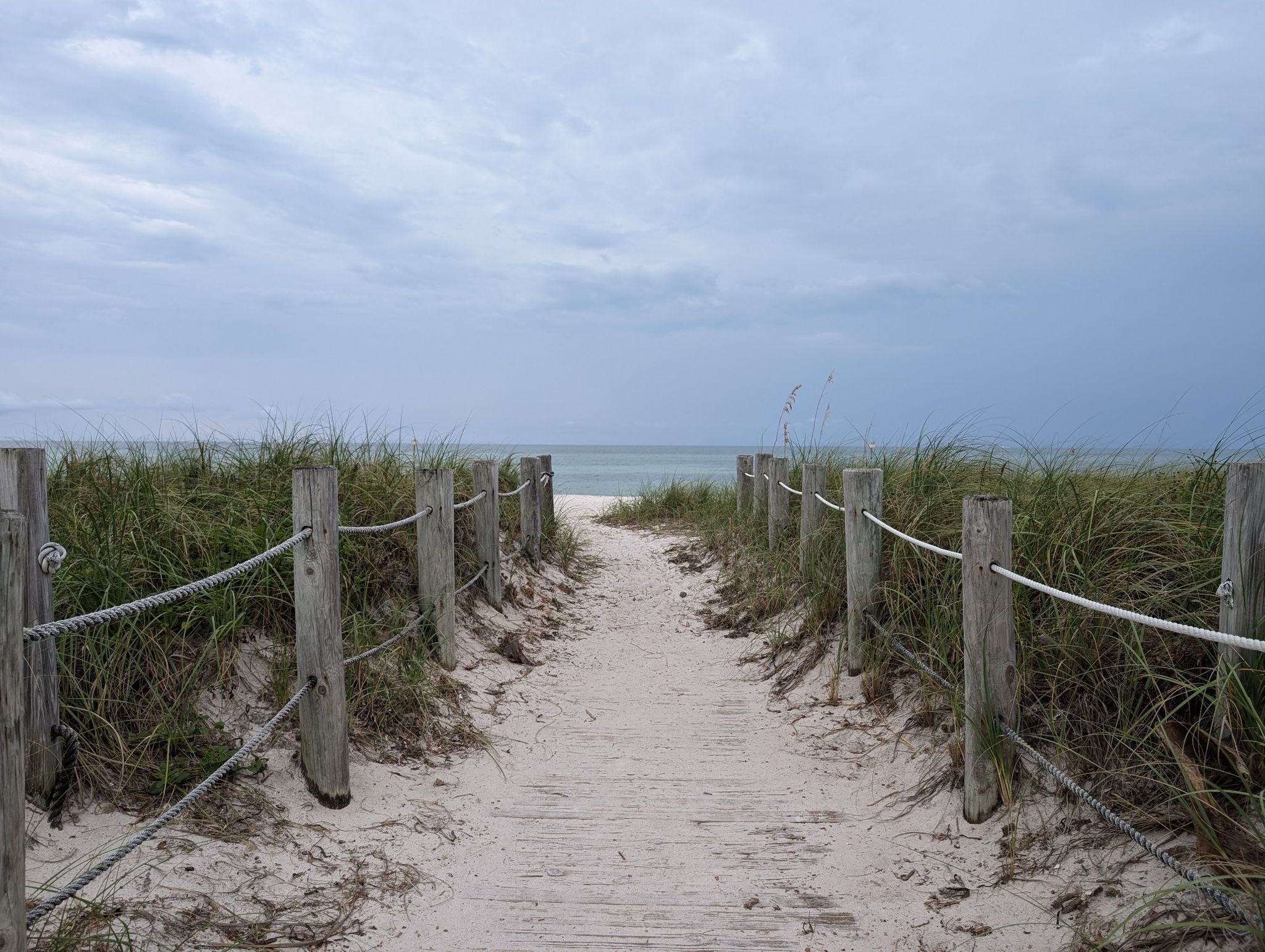 Sandy path with rope fences leading to a calm ocean under cloudy sky. - Key West Cycling Loop