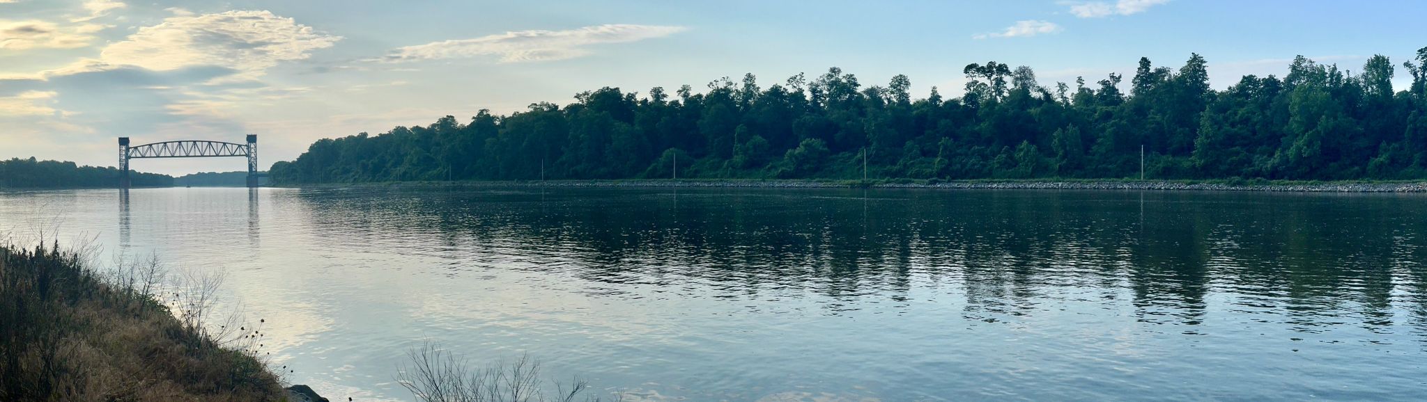 A wide river reflects the sky, with a distant truss bridge and forested banks. - Michael N. Castle C&D Canal Trail