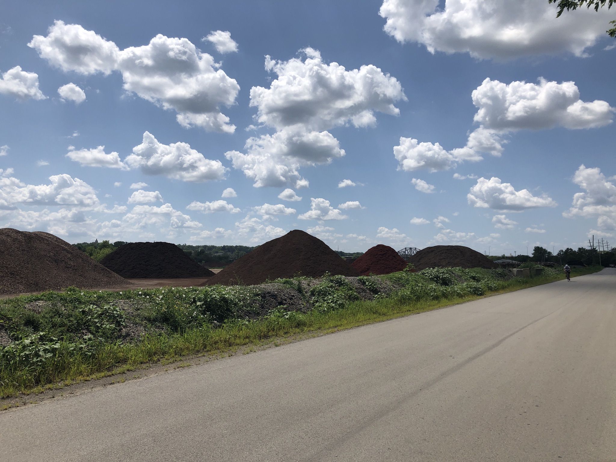 Large dirt piles beside a paved road under a bright, cloudy sky. - Centennial Trail – Keepataw Reserve loop from Lemont